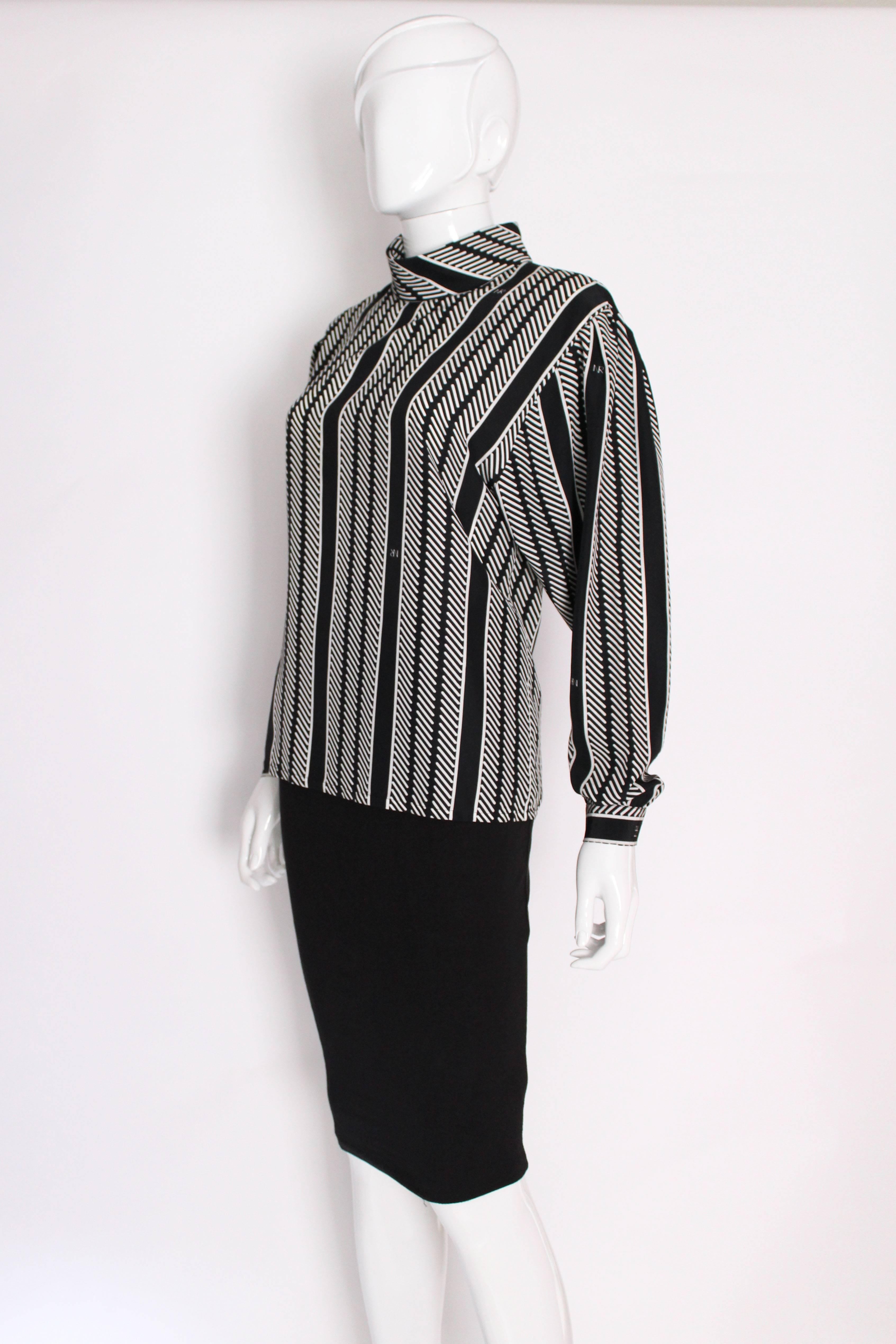 A stylish blouse by Nina Ricci , Paris. With a black background and white strip detail, plus a few subtle 'NR's', this blouse is easy to wear. It has a foldover , mandarin style collar and button opening at  the back.There is a button opening on
