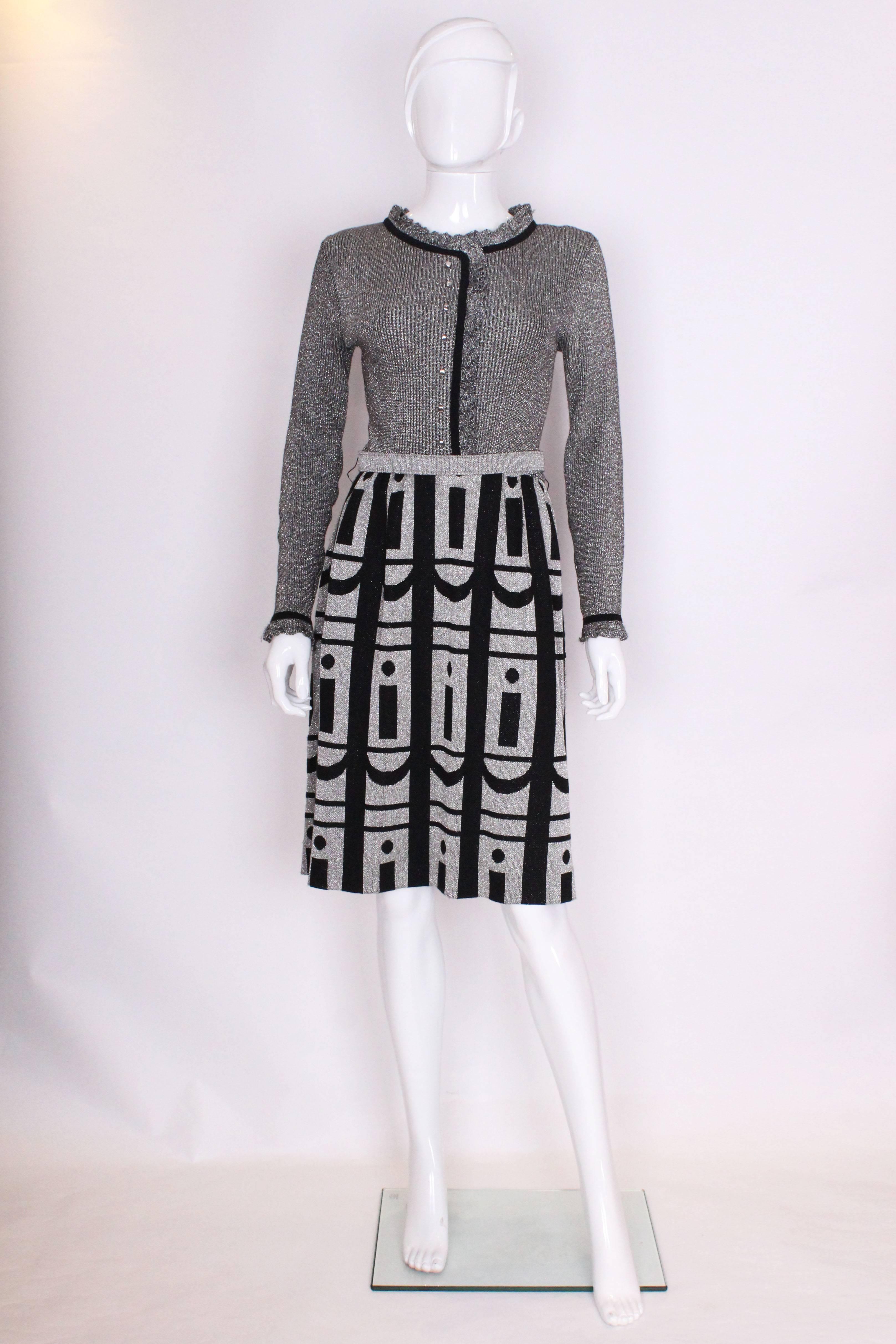 A great , cocktail dress by Louis Feraud at Rembrant.The bodice is silver with a ribbing detail and a frill at the neck, front and cuffs.The skirt is gathered and  has a sliver and black geometric print, silver belt and back zip.The dress is sized