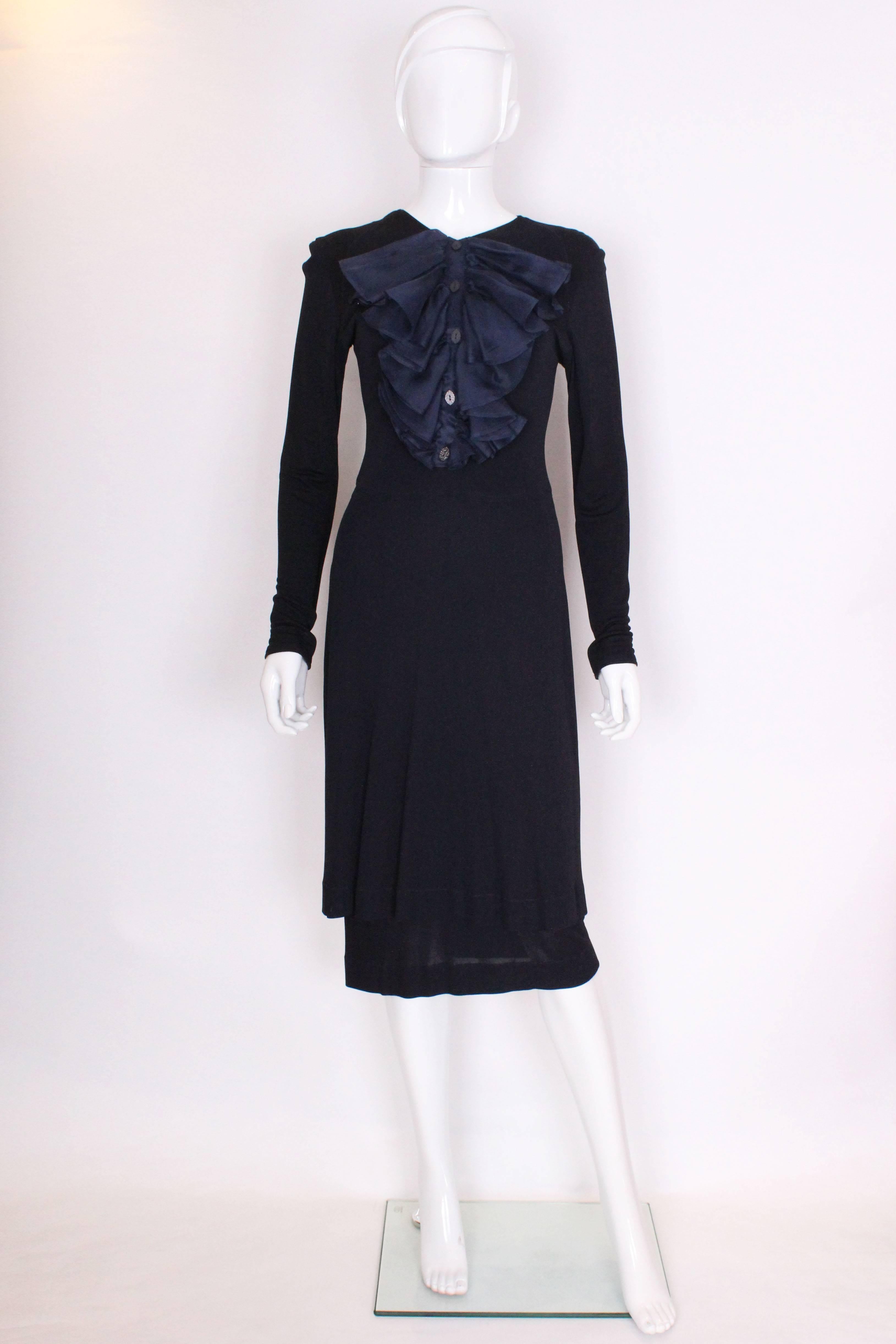 A charming and chic dinner dress by British designer Jean Muir. In a wonderful ink blue colour, this dress has a slight v neckline, with a large frill on the front with 5 buttons. The skirt  has a double layer of viscose so it hangs beautifully and