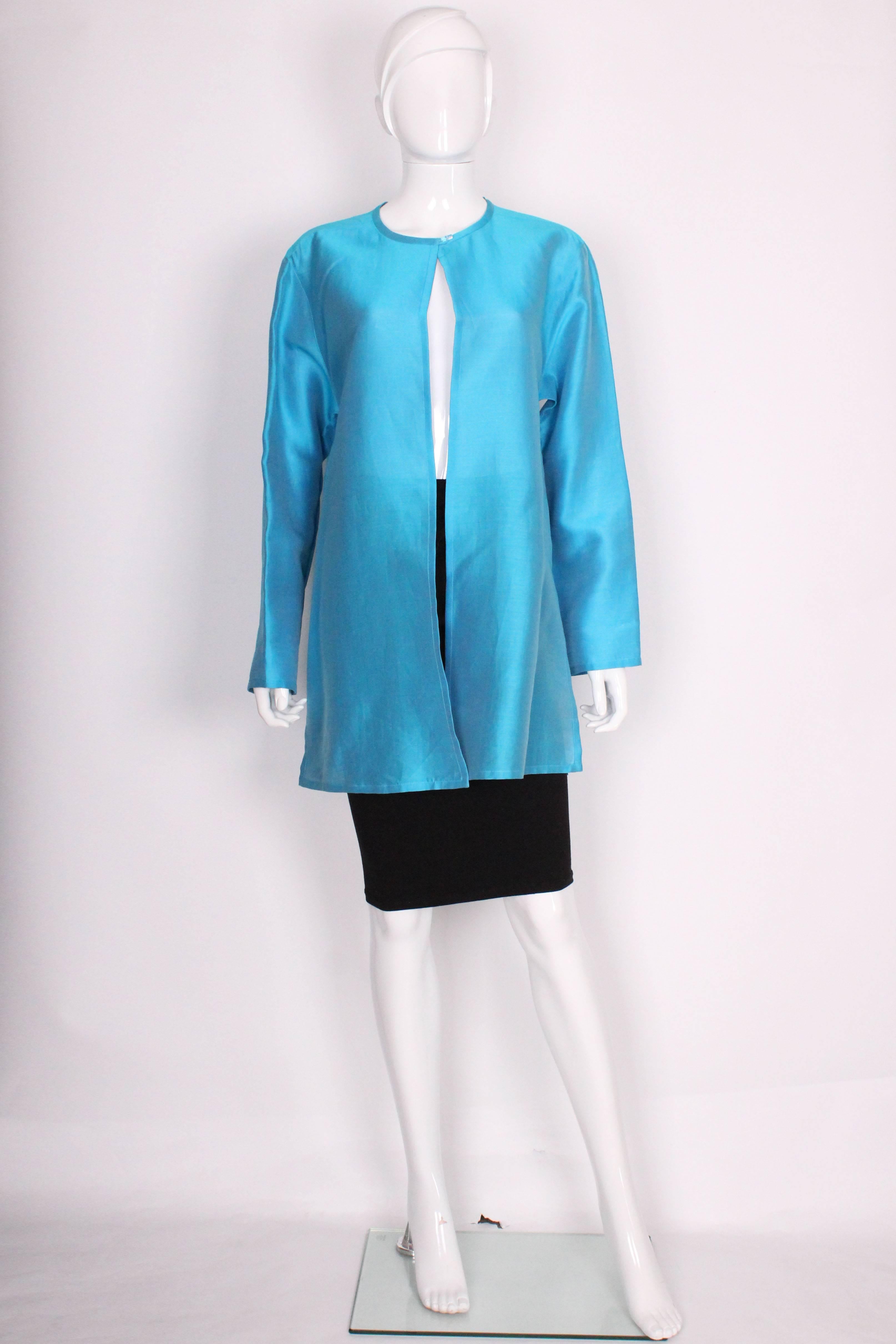 A stunning jacket by British designer Jean Muir.In an stunning turquoise colour with dark blue lining, this jacket will brighten up any outfit. The jacket has a round collar,with a one button fastening at the neck. There is a 11 1/2 slit on either