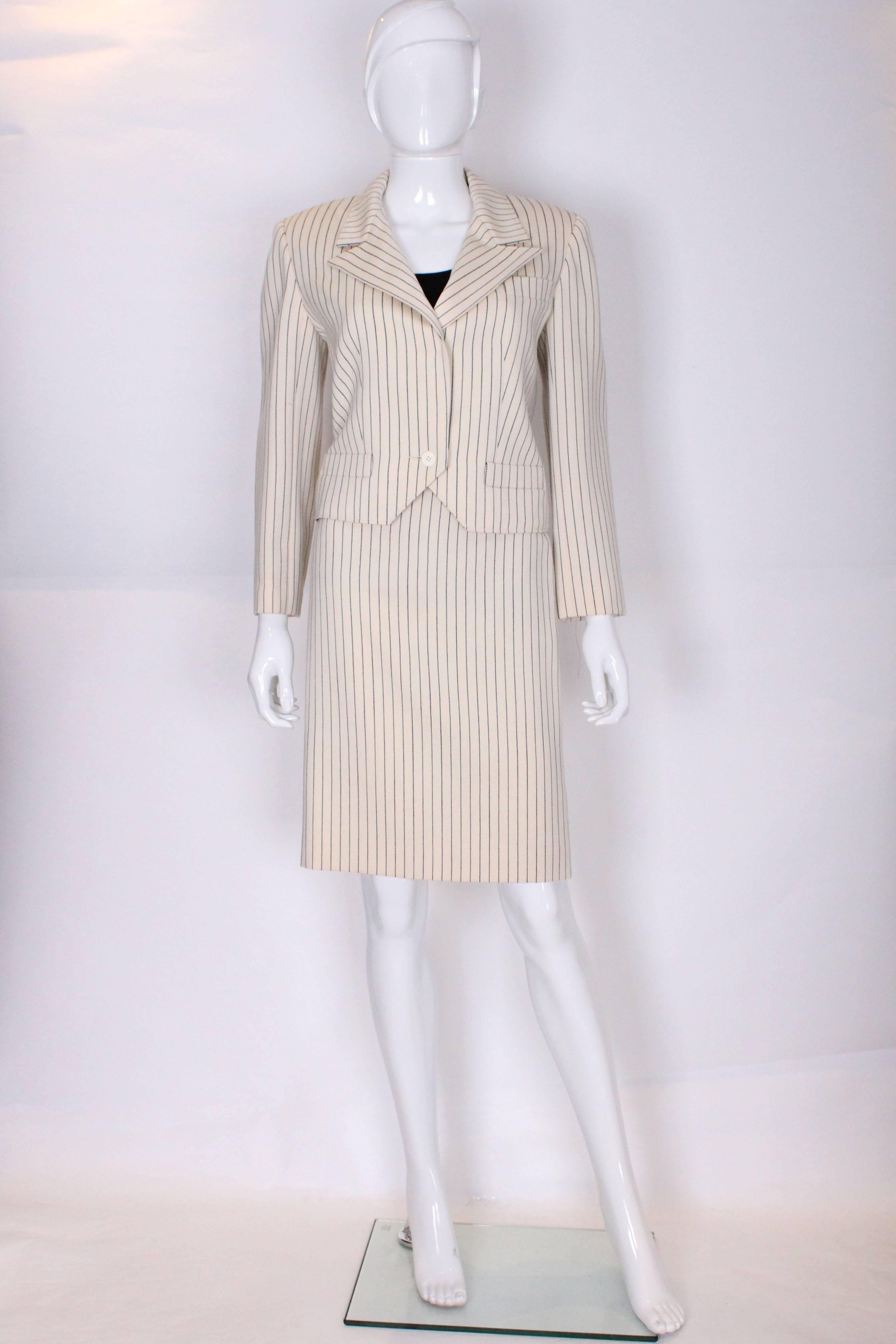 A chic skirt suit by Christian Dior, in a cream wool with a black stripe.
The jacket is tuxedo style with a cut away front, with two pockets at waist leval and one on the left breast pocket. The jacket fastens with one button.
The skirt has a