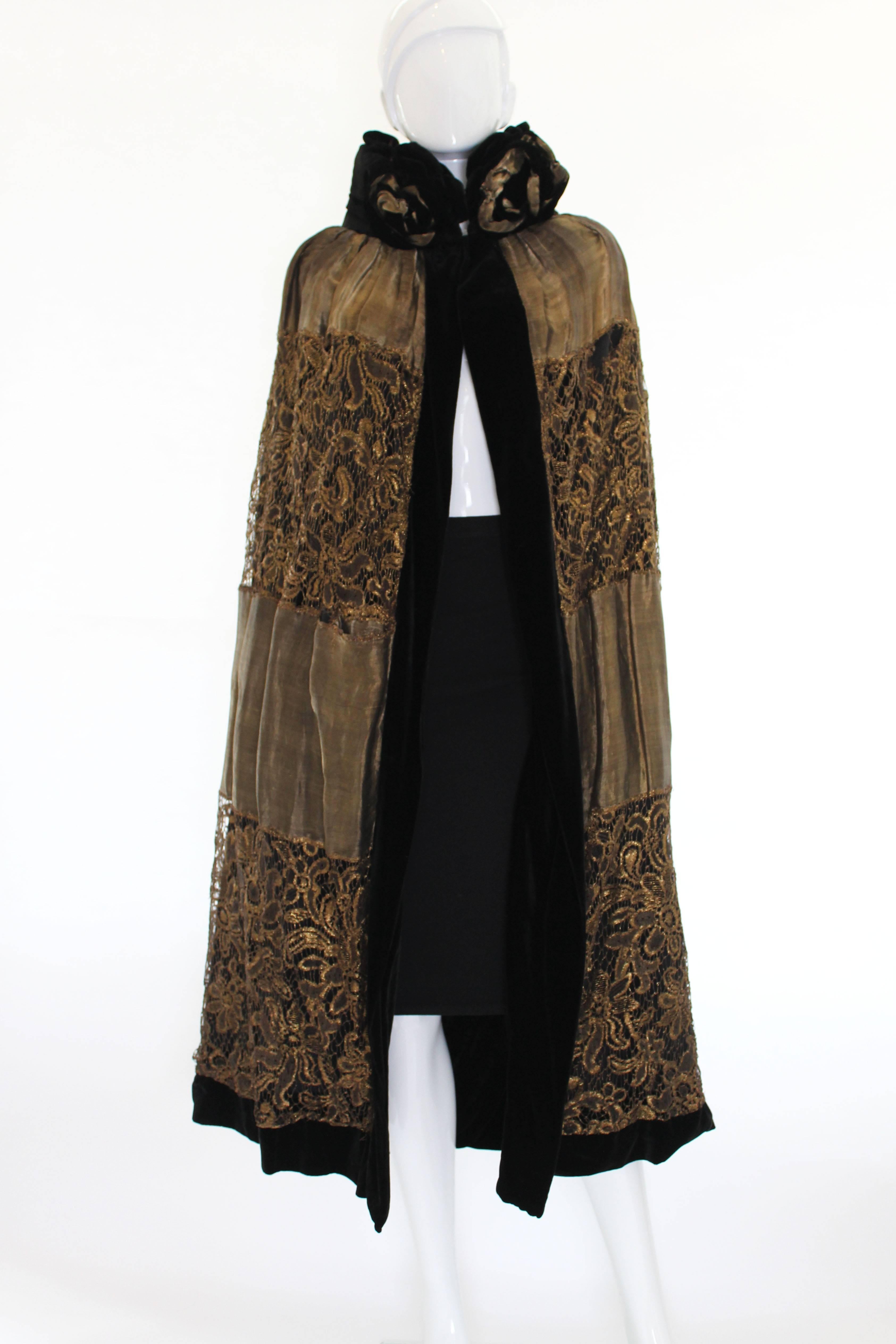 A divine 1920s evening cape made of a luxurious black velvet and lined in an amazing gold lame lace. The collar of this cape has wonderful black velvet and gold lame roses around it that come up to your chin. The inside is lined in alternating bands