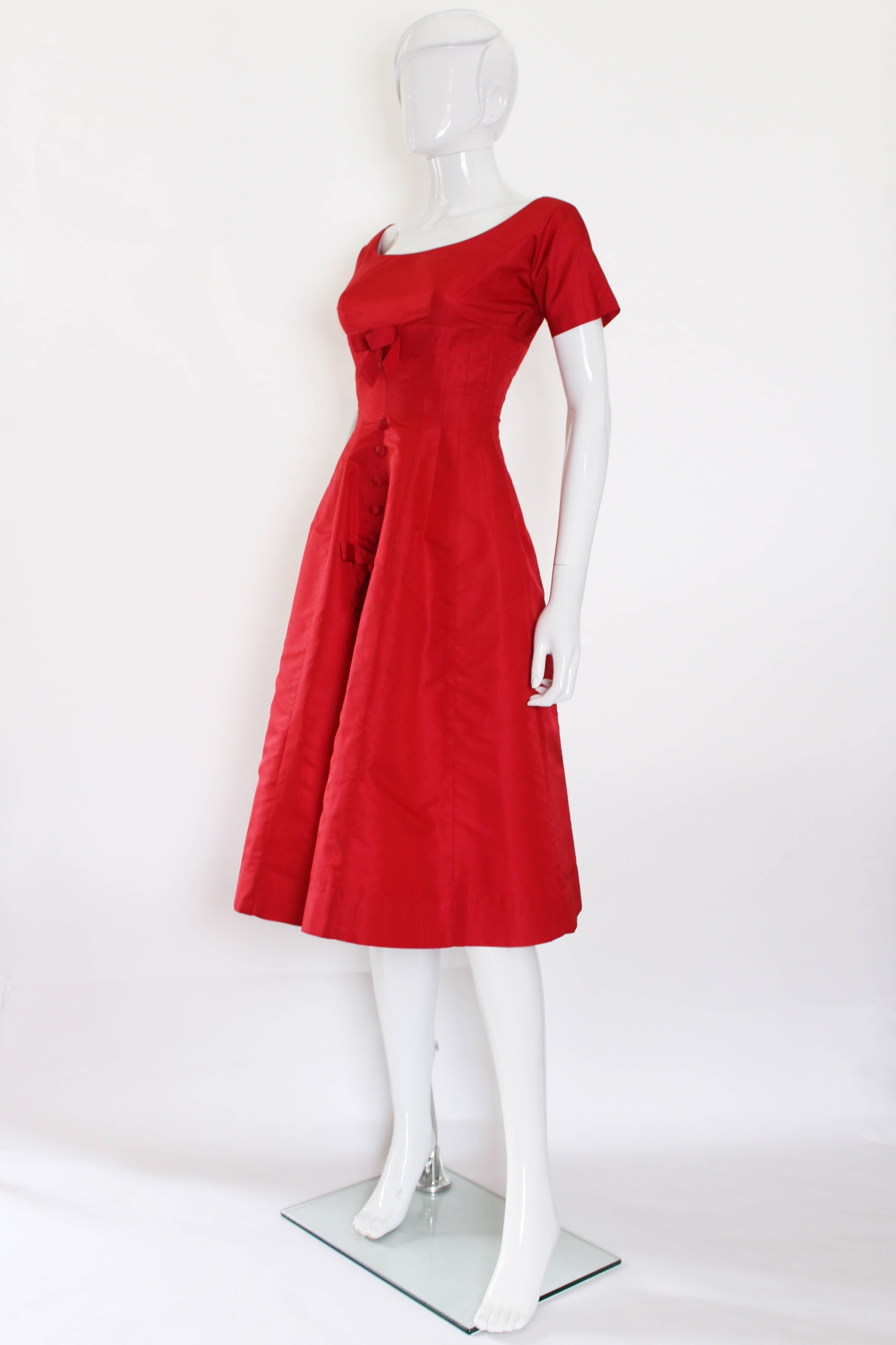 

This stunning 1950s party dress has an amazing shape and structure to it. The waist is drawn right in with 20 panels making up the dress from the bust, that flutes out from the waist to give great volume. The front has two bows and five buttons