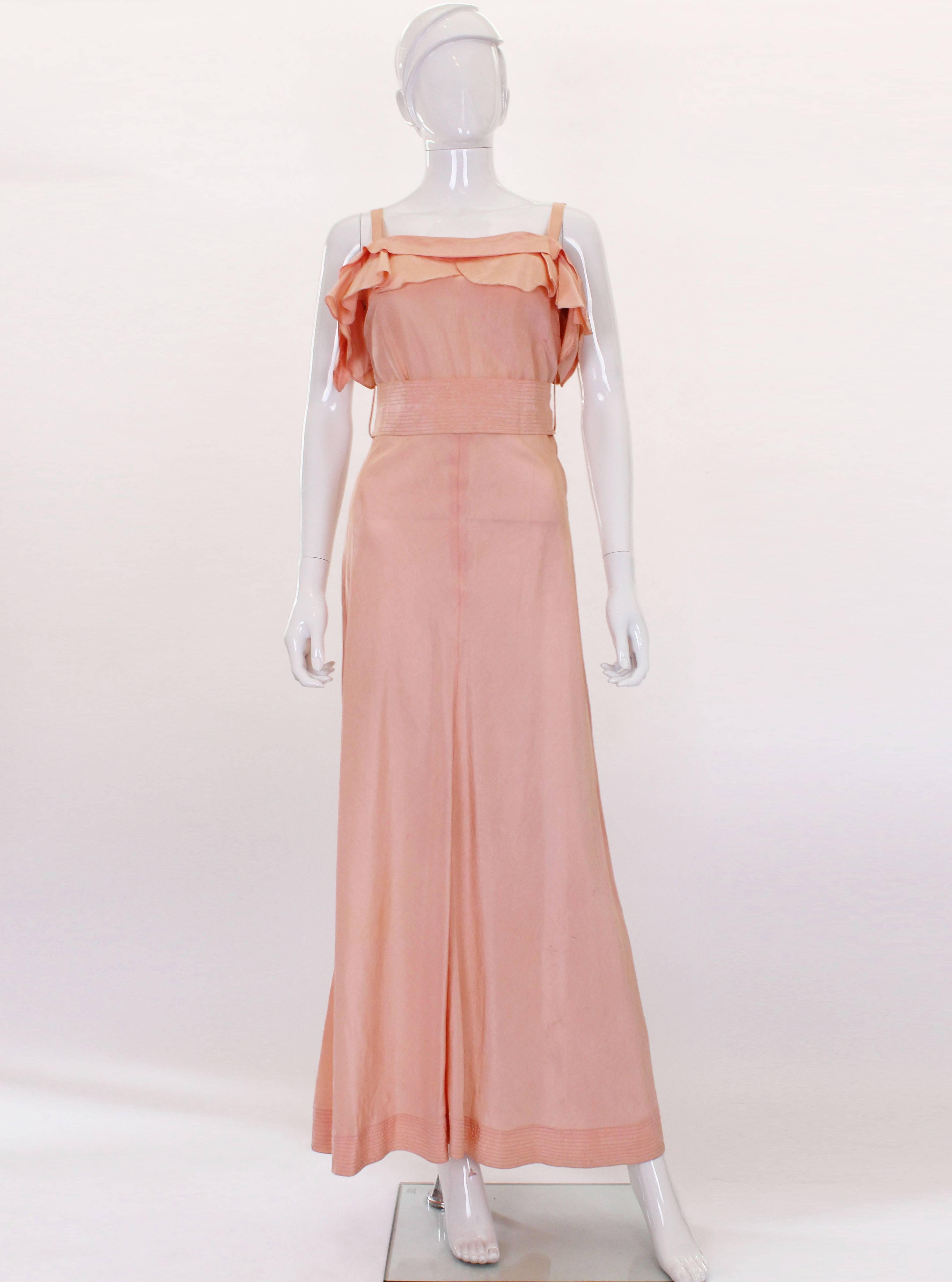 A stunning soft peach silk gown in exceptional condition from the 1940s. The dress has thin straps, with two layers of frills on the front and back of the neck. It opens with poppers down the side. The skirt of the dress flares out slightly and
