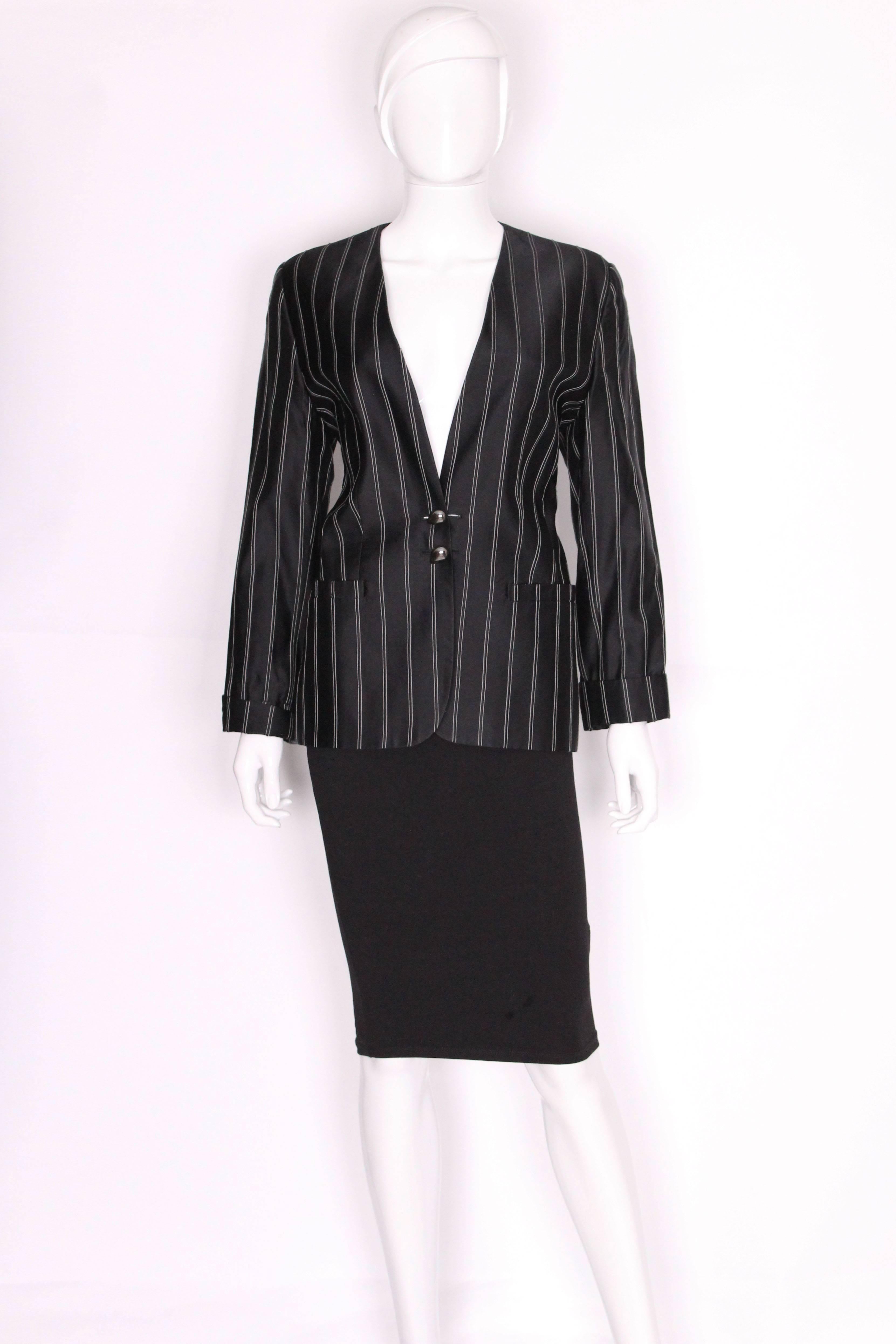A chic jacket by Gucci. The jacket is made of a black silk mix fabric with white double stripes.It is collarless and has a deep v neckline.It has turn up cuffs, pockets at waist level and a two button fastening.