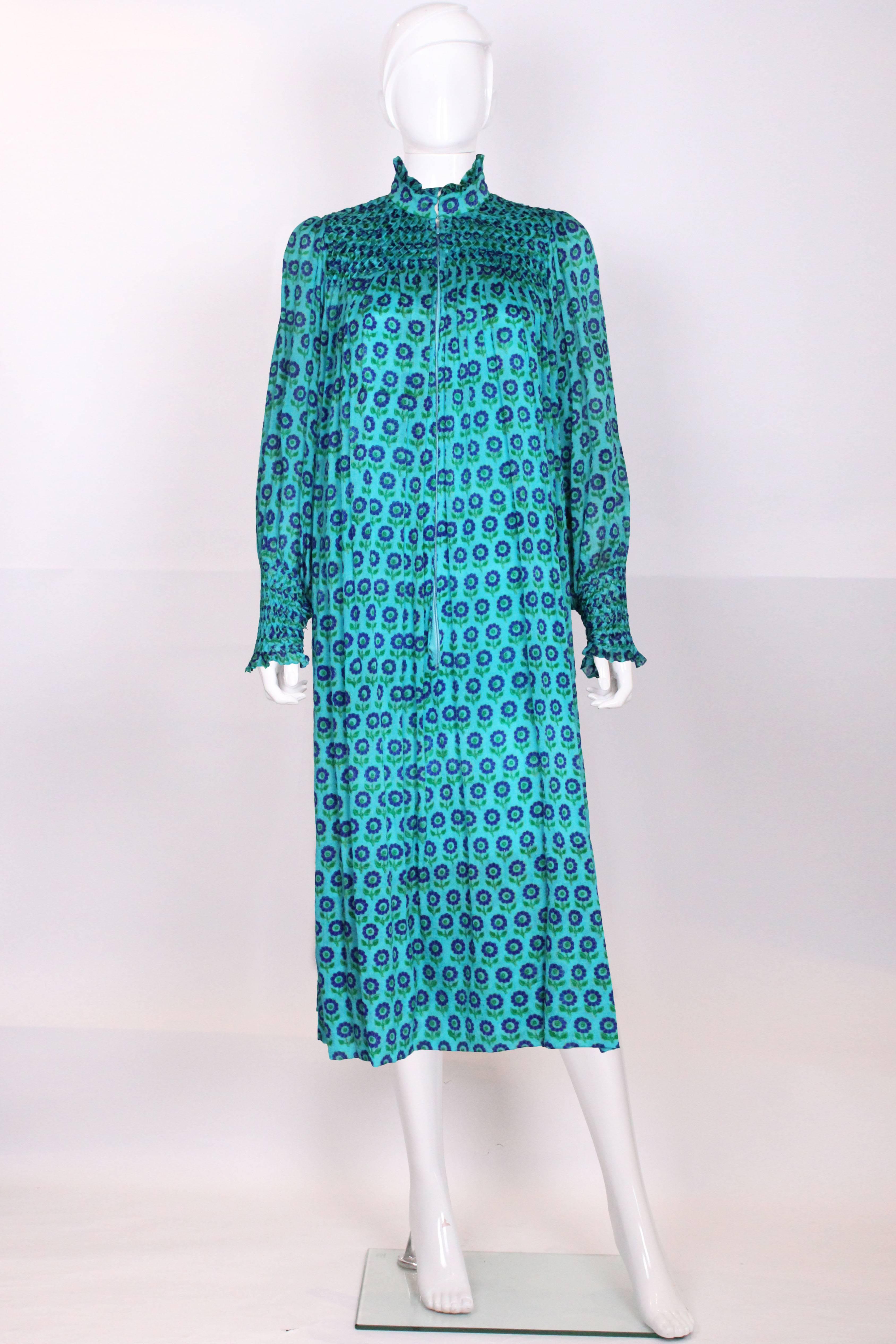 A charming silk dress from the 1970s made for Harrods. The fabric is a beautiful turquoise silk, with a floral design of purple petal flowers. The dress has a stand up pie crust collar,and there is wonderful smoking on the yoke and cuffs. The dress