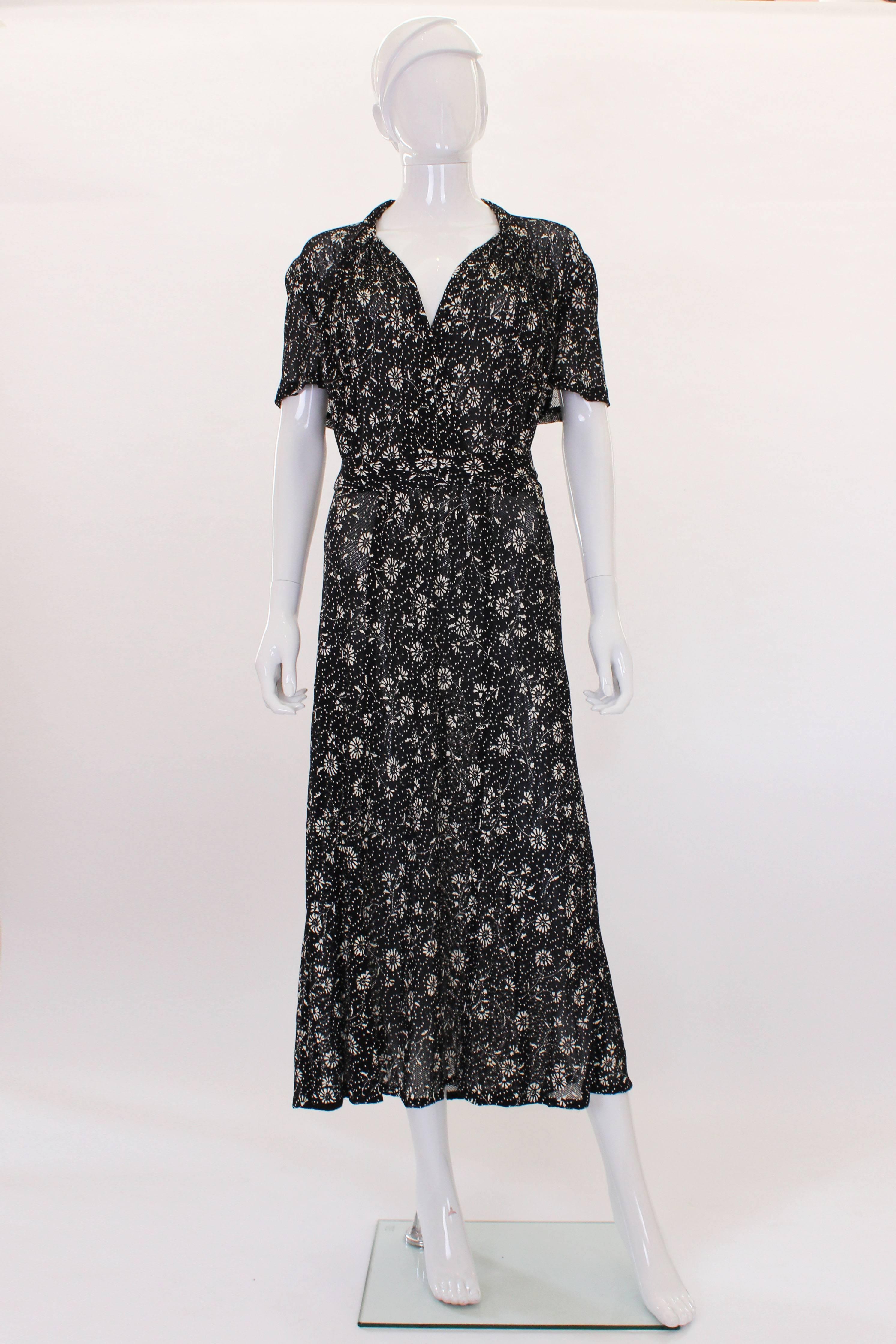 This 1940s dress is quite an unusual piece. The fabric of the dress is a dense very dark navy mesh with an ivory floral print that is stencil printed on. The top of the dress has some rouching over the bust. There are small circular cut out that the