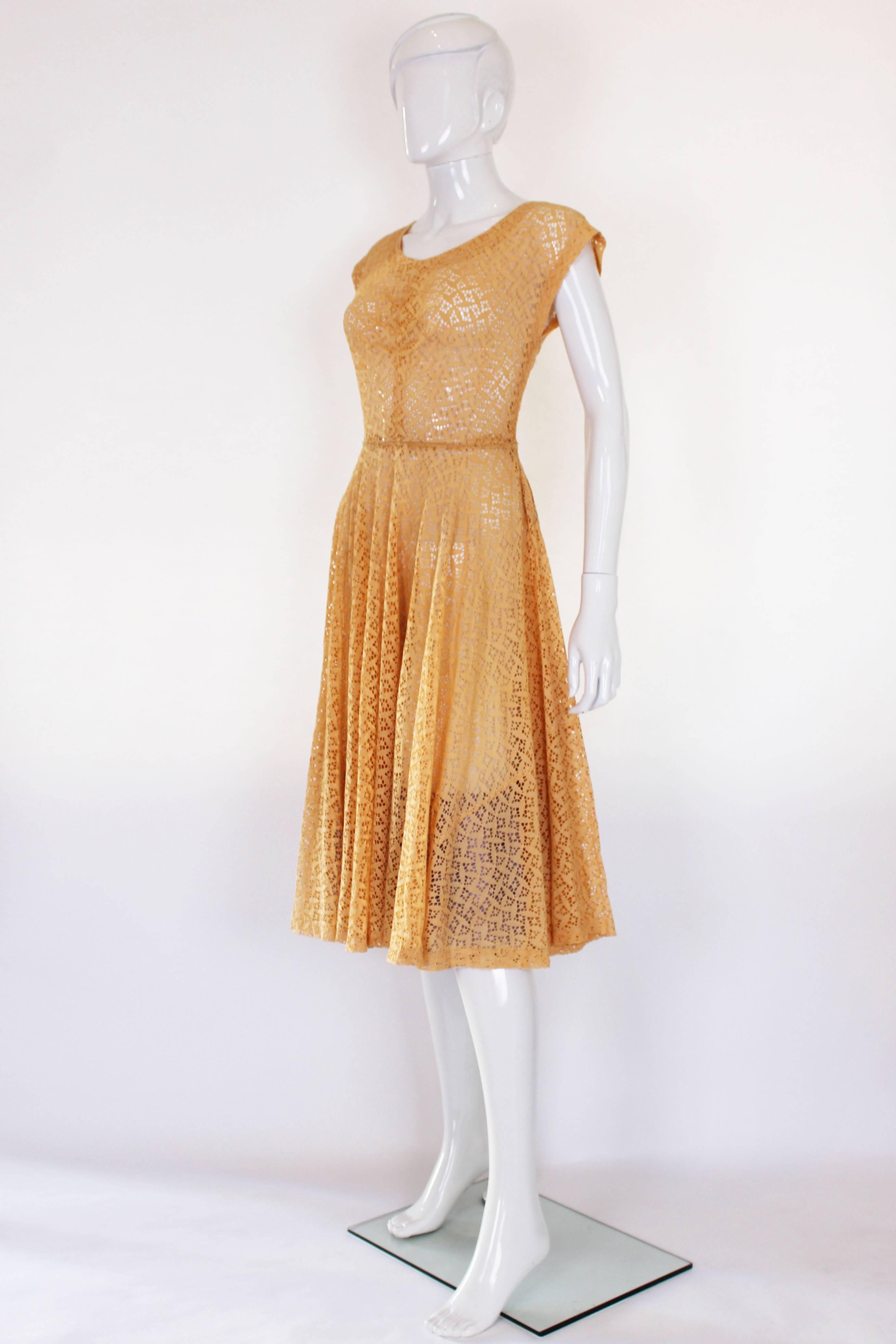 This is a classic 1950s style dress made of an apricot coloured cotton. The fabric is made up of diamond shapes with Broderie Anglaise cut outs so a slip needs to be worn underneath. The bust has a small amount of ruching that gives it shape and the