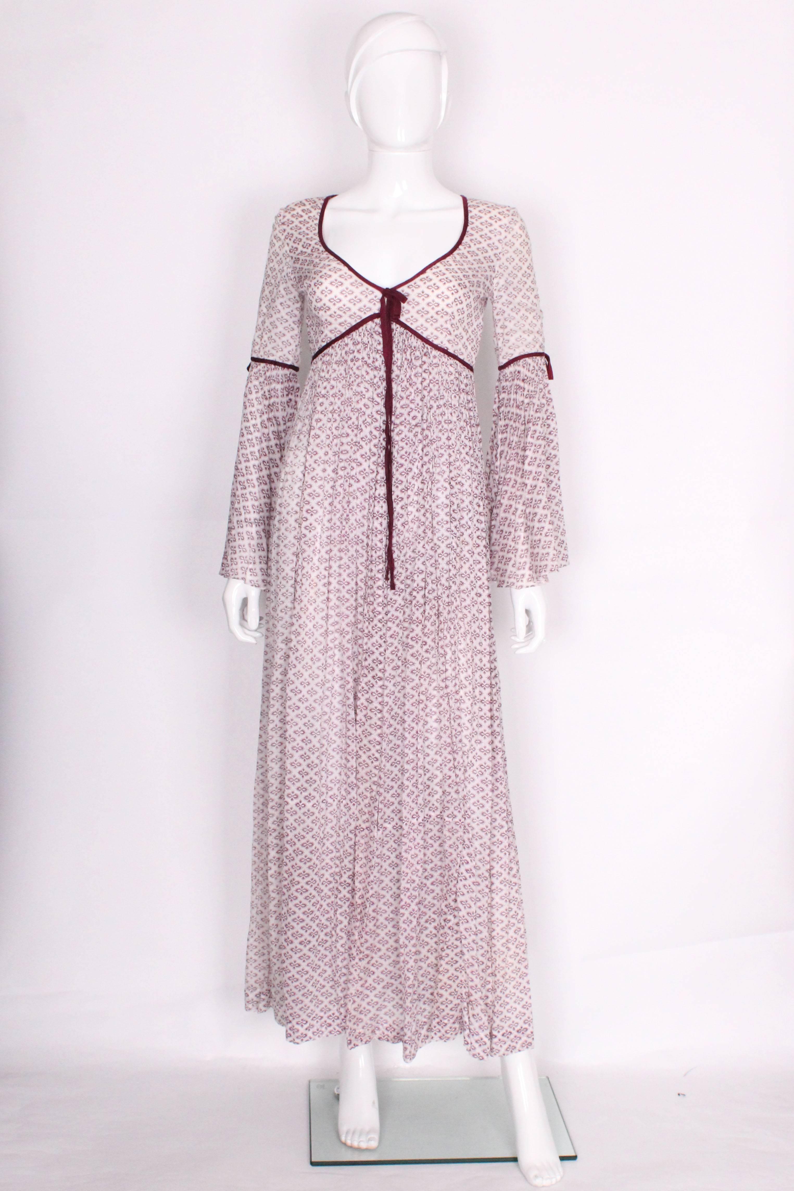 This is a great boho maxi dress by British designer Colin Glascoe. Made of several layers of fine cotton, the outerlayer is white with a geometric burgundy print, and the inner layer is also white cotton. The dress has a v-neckline edged in a dark