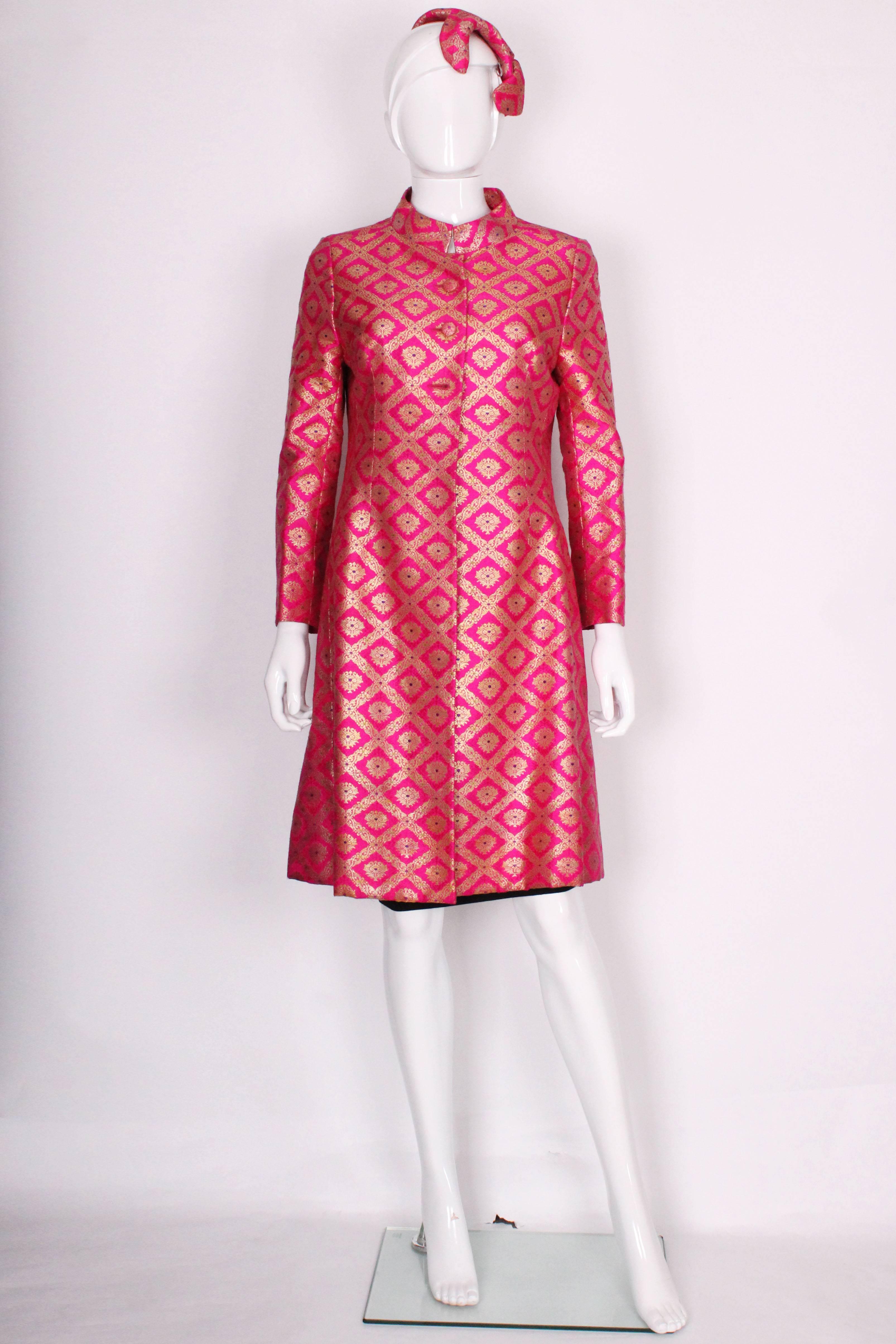 A stunning silk coat in a bright pink with gold jaquard detail and small flecks of other colours. The silk lining is a rich, bright purple which sets off the fabric of the coat beautifully. There is a manderine style, stand up collar, and 3 large