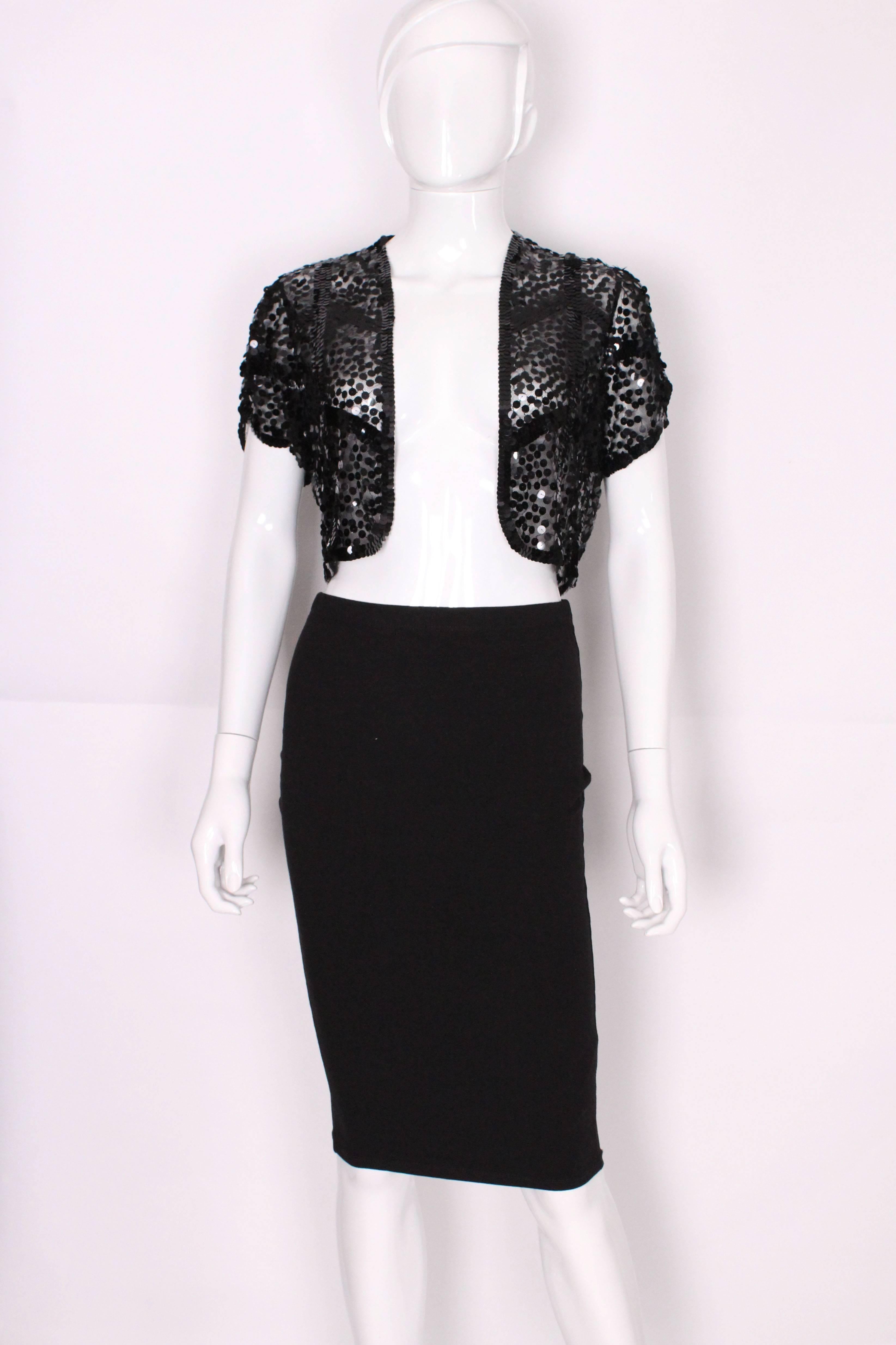 This is a great little black net bolero jacket embellished in flat black high shine sequins. A really nice piece to go over a party dress or top. The sequins are sewn in a bold chevron shape across the top which makes it quite modern looking. The