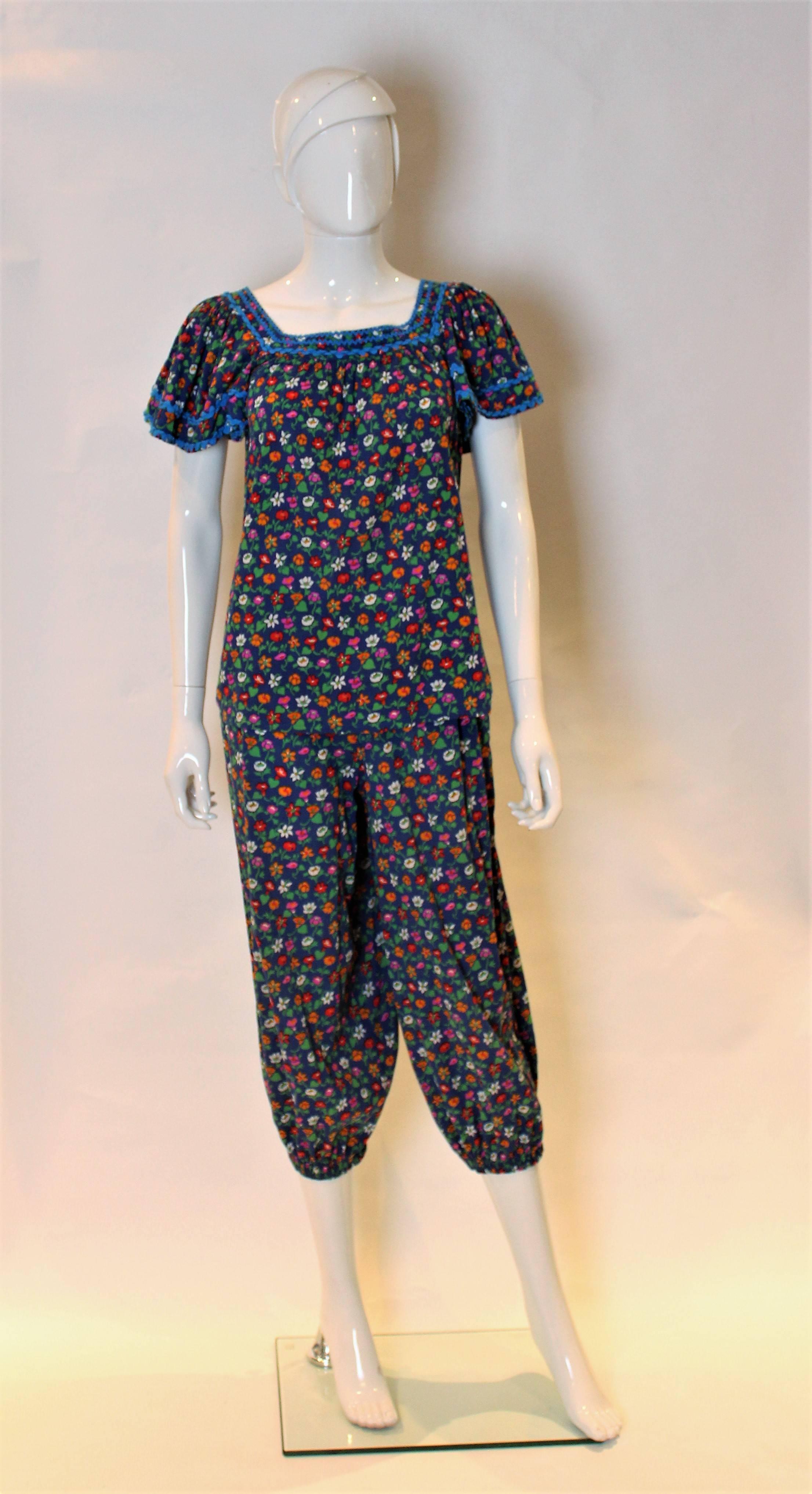 A great outfit for Spring/Summer. This outfit comprises , a short sleeve smock like top , and nicker bocker like trousers. The background is dark blue with a floral pattern in orange, pink, red , whte and green.The top has electric blue trim around