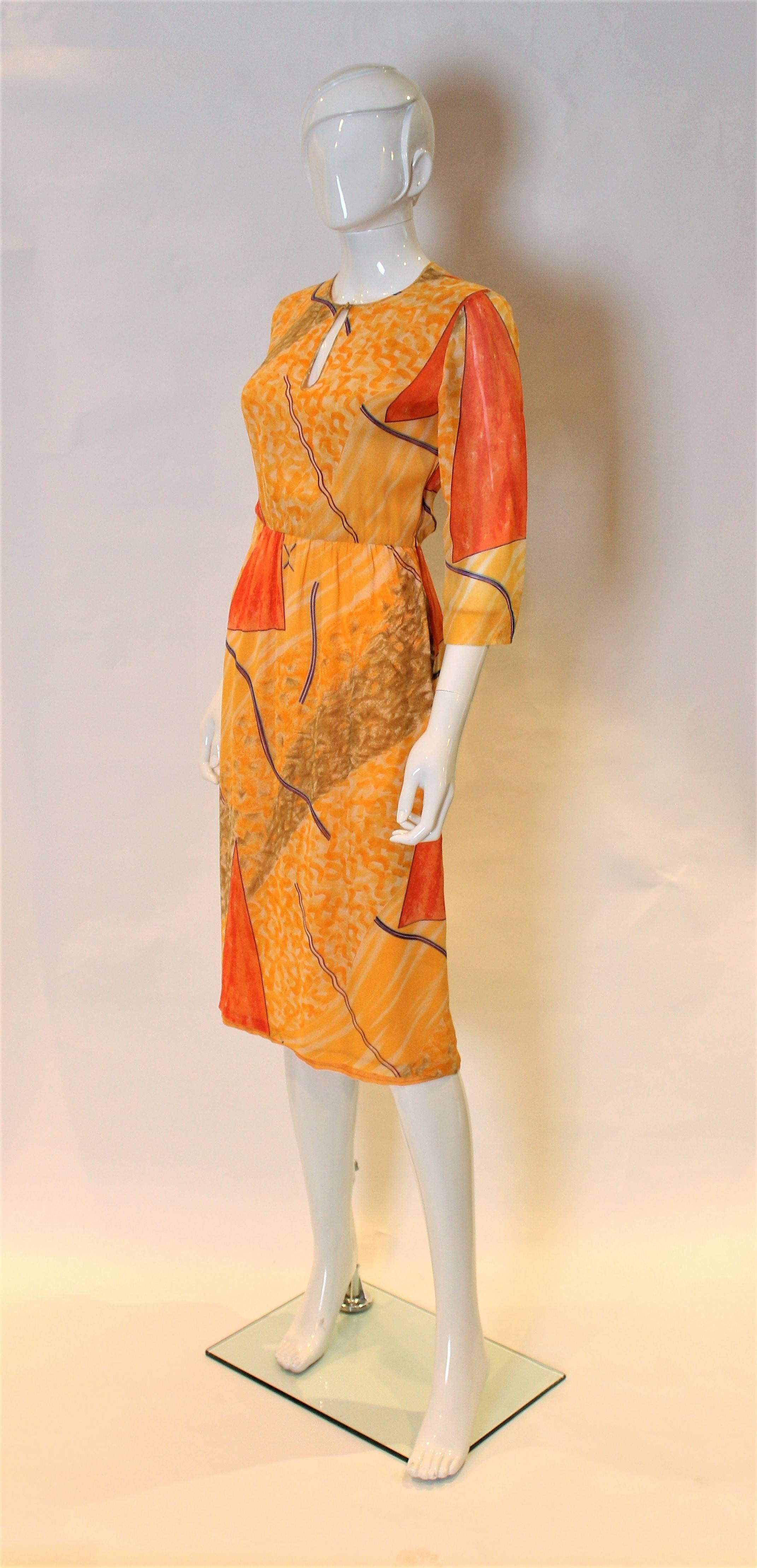 A great dress by Chanel Creations. In a multi colour silk chiffon,shades of orange,olive, blue , and aubergine.The dress has a key hole neckline, side zip and elbow length sleeves. The top half is lined in silk chiffon and the bottom in sik.
