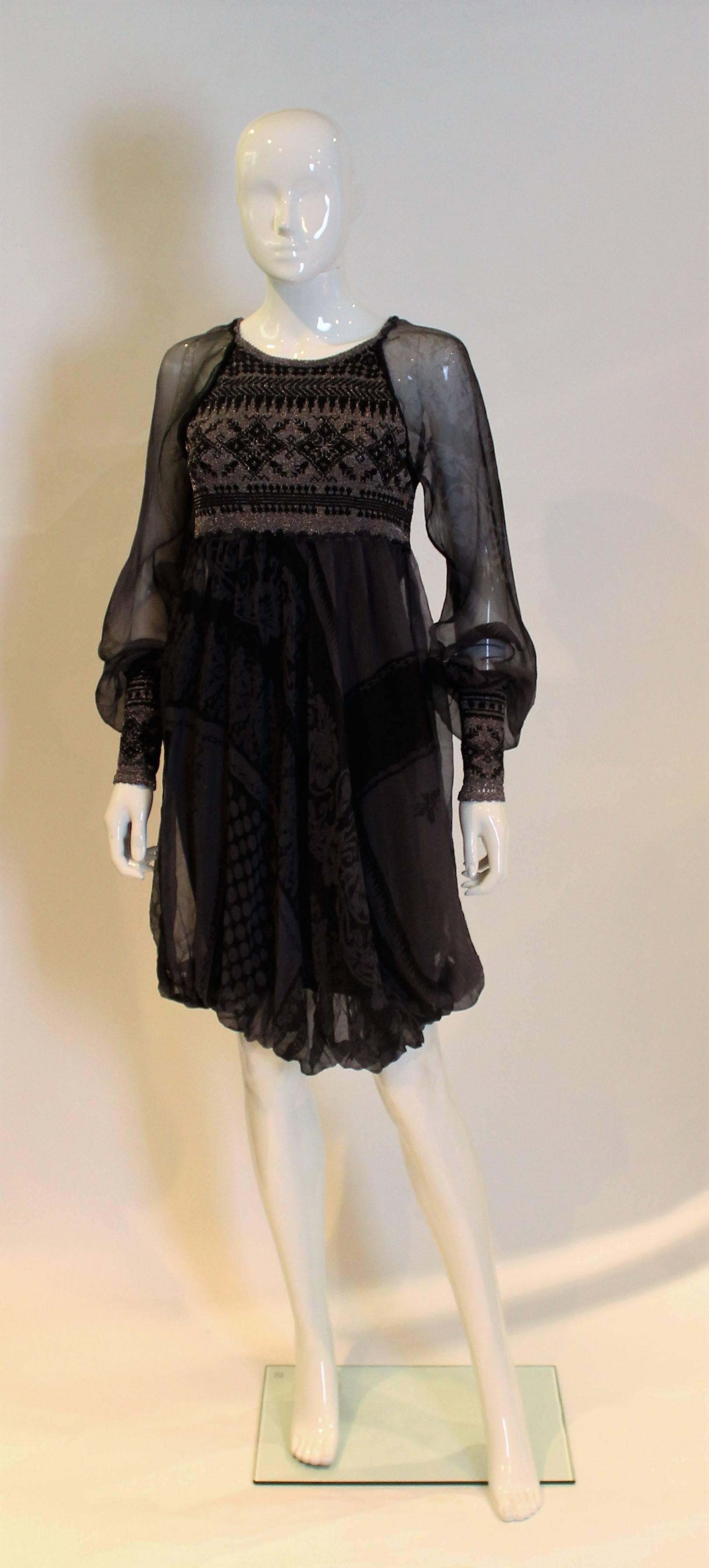 A chic dress by Jean Paul Gaultier. The trunk of the dress is knitted , in black and silver. The sleeves are silk, and there is a silk over skirt over the kitted body.The dress has elegent 6'' wide cuffs and a tie opening at the back.