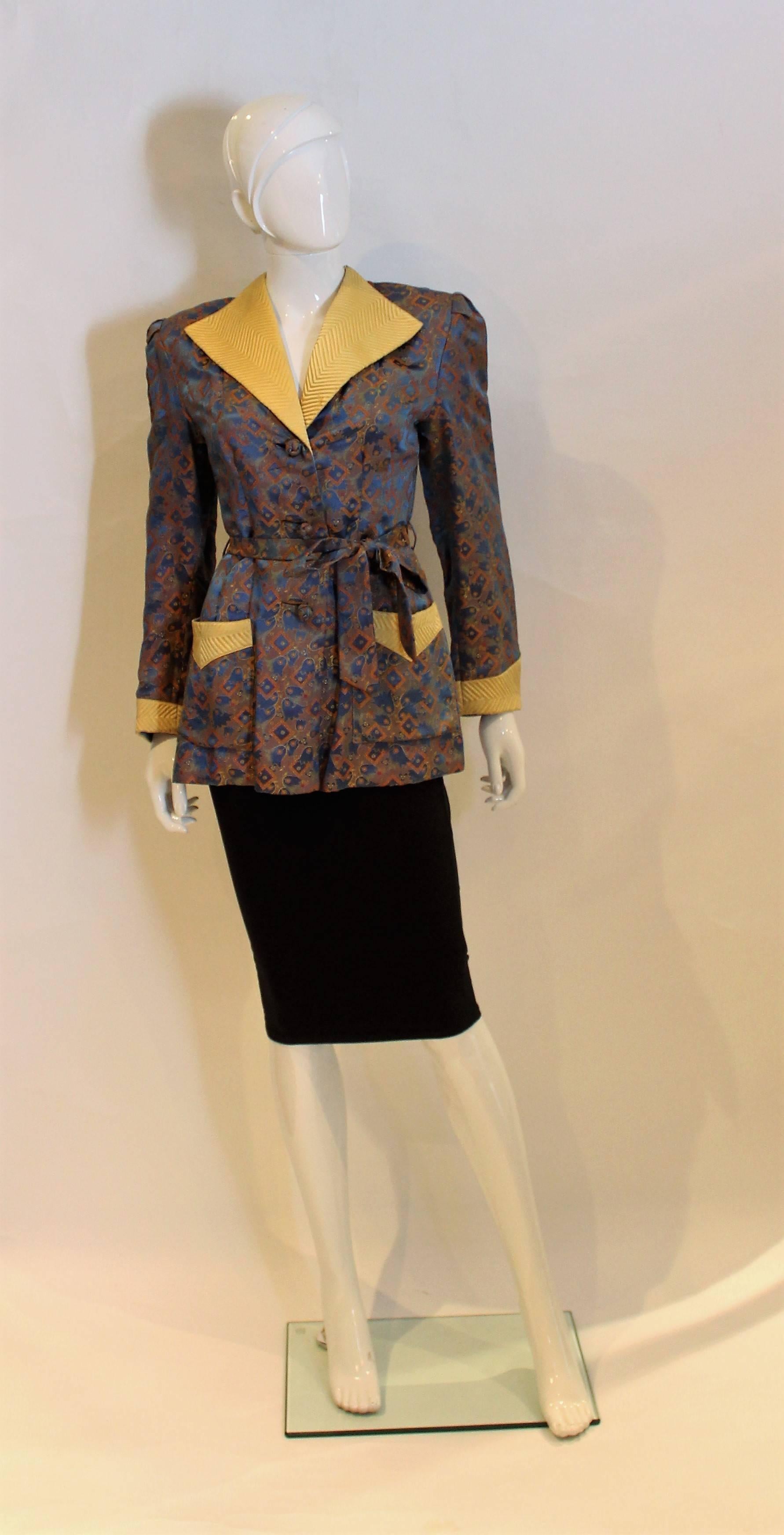 A chic Chinese Silk jacket. This jacket has gold cuffs and collar, and pocket detail.It opens with three silk knot buttons and has a same fabric tie belt.