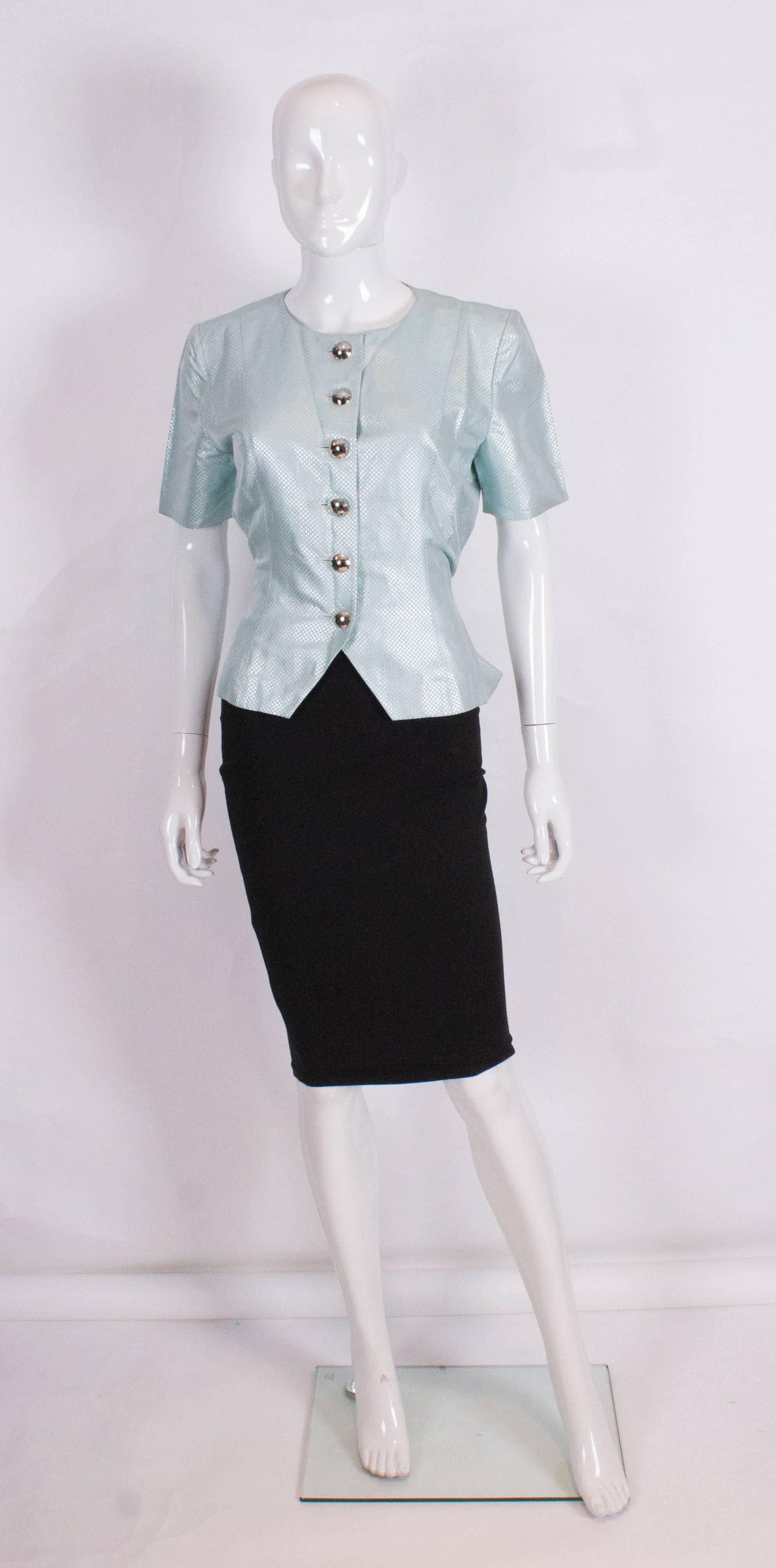 
A chic jacket by Yves Saint Laurent , Variation line. In a silver and blue check, the jacket has a round neck, short sleeves,button front with cut out detail , a pleated peplum at the back, with a self fabric tie belt.
