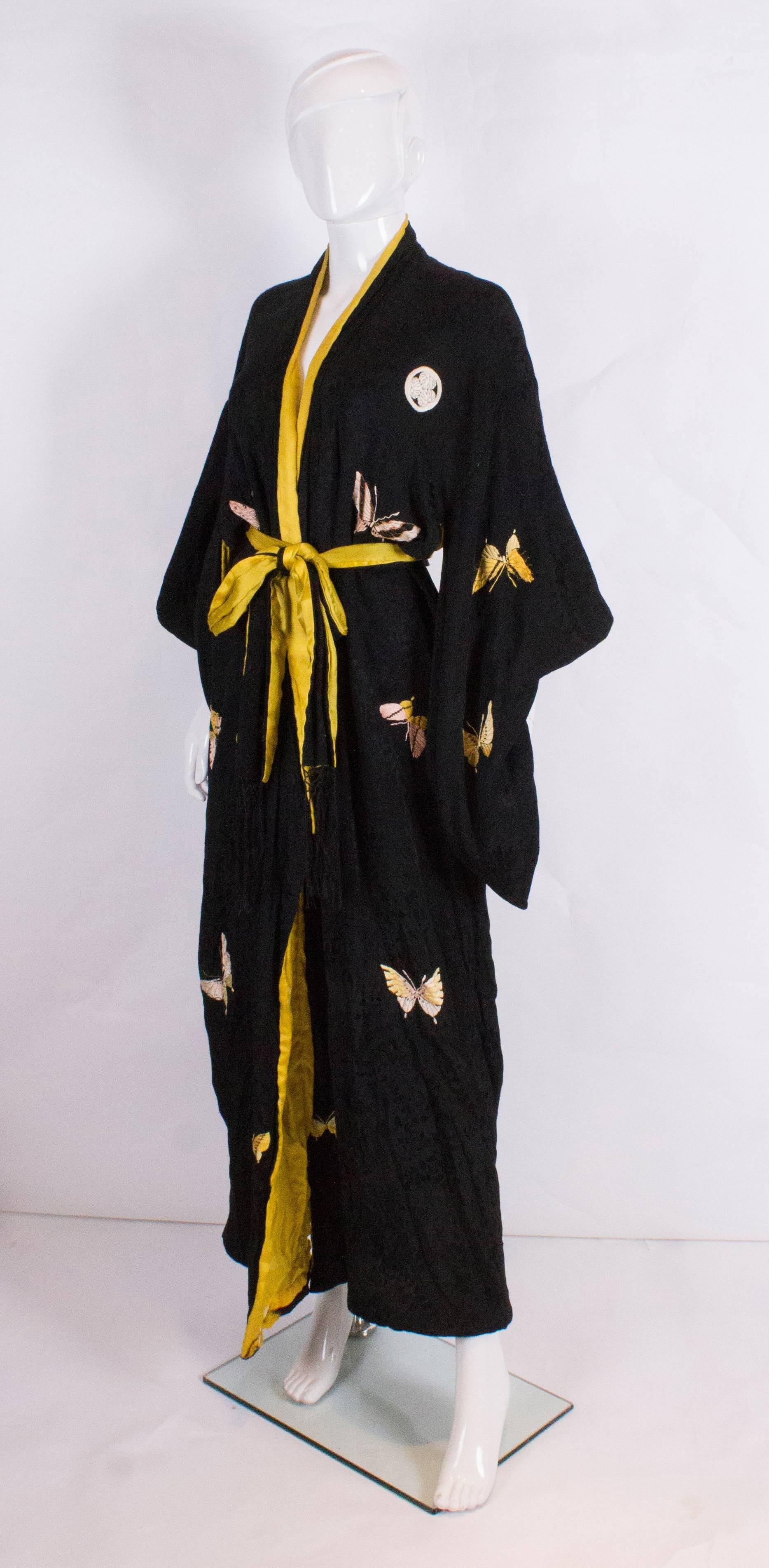 A super kimono from the 1920's. In black silk with a bright yellow lining, the kimono is embroidered with butterflies in pink and yellow.It has a black silk belt with fringing and butterfly detail.Bust up to 48