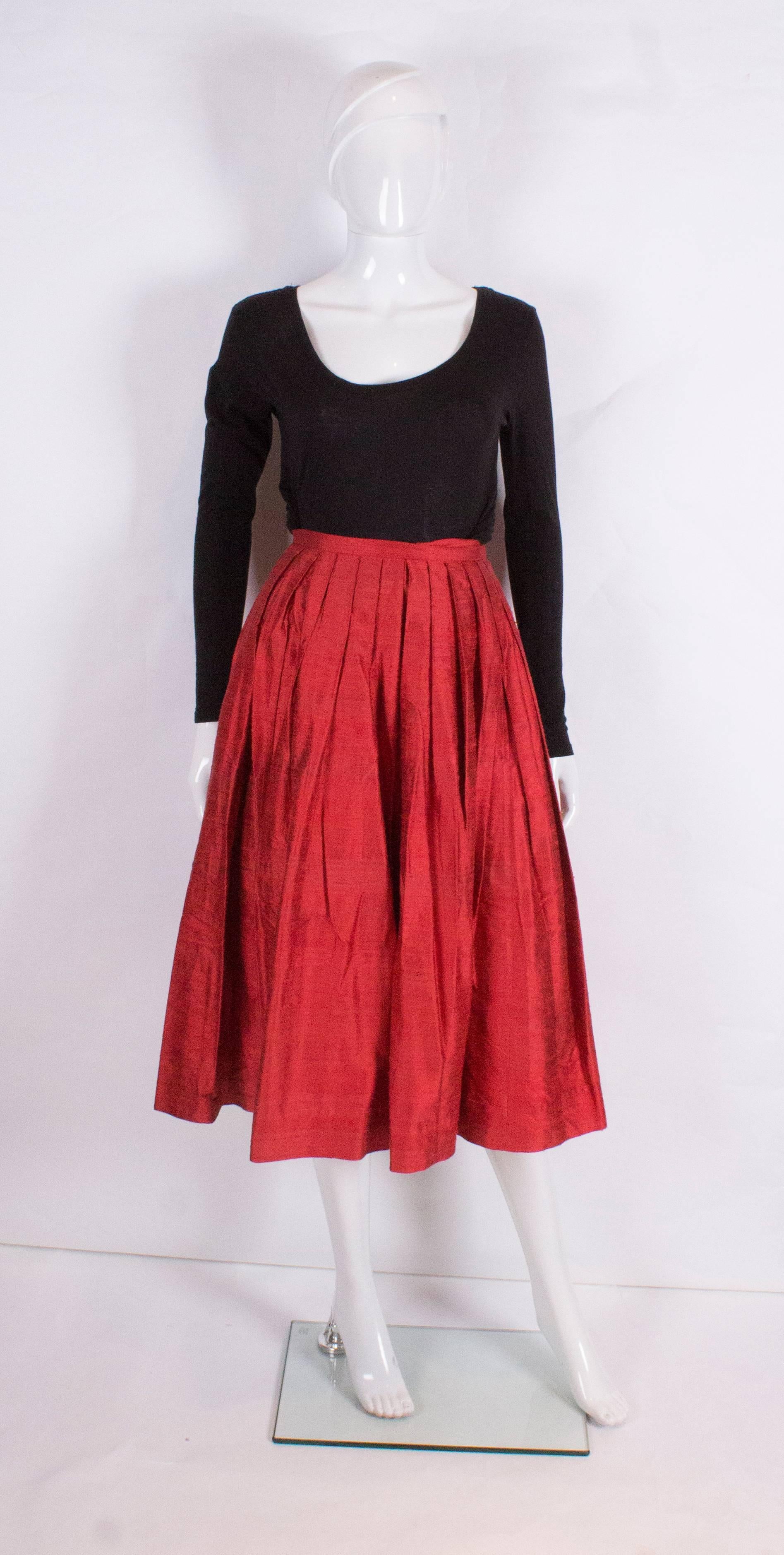 A great skirt by Caroline Charles. In a tomato red raw silk, the skirt is gathered and  pleated from the waist band .The skirt is fully lined and has a 2 1/2 hem.