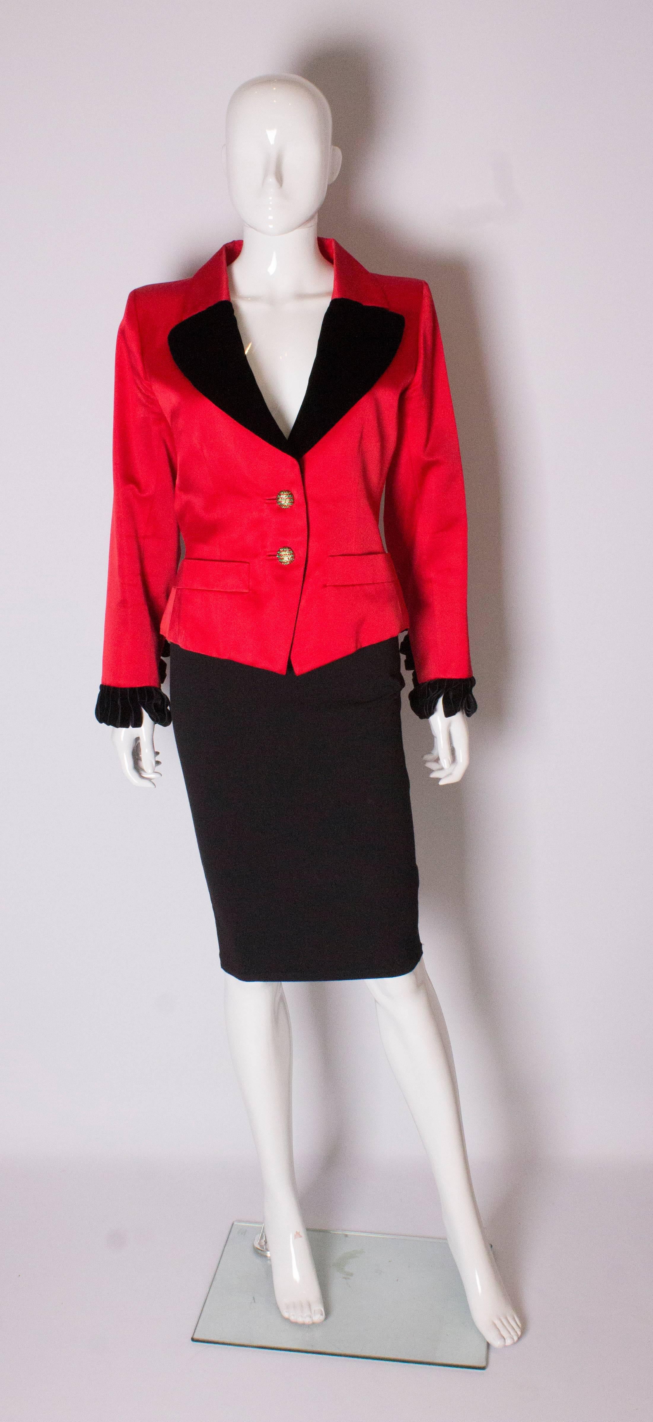A red evening jacket by Yves Saint Laurent Rive Gauche. The red jacket has a red and black collar with black velvet frill cuffs and velvet ties at the back. It has a two button opening and pockets at waist level.