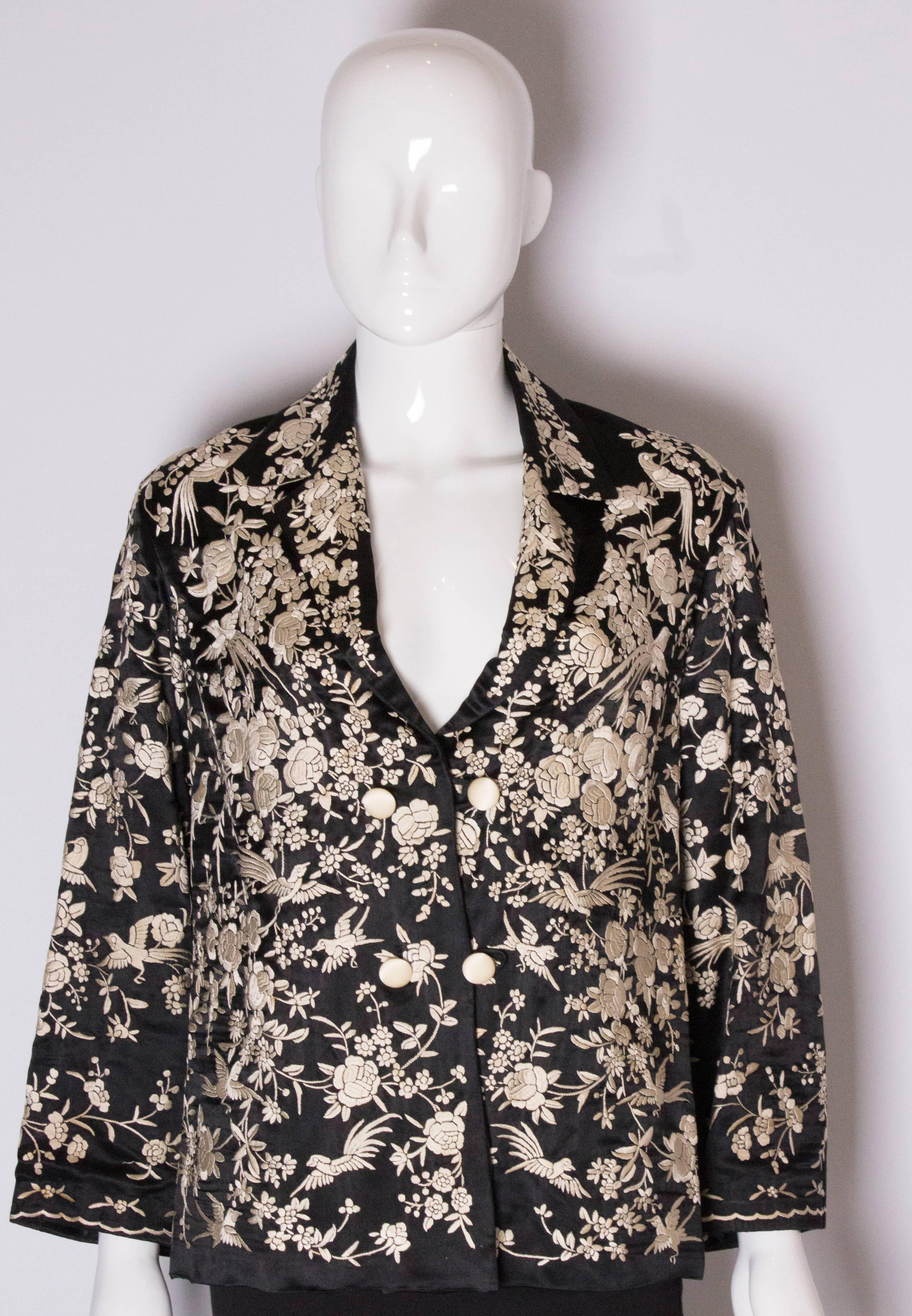 A chic Chinese jacket  in black silk with white embroidery , in a bird and flower design.
The jacket has a cutaway collar and two button fastening, and is lined in white silk.