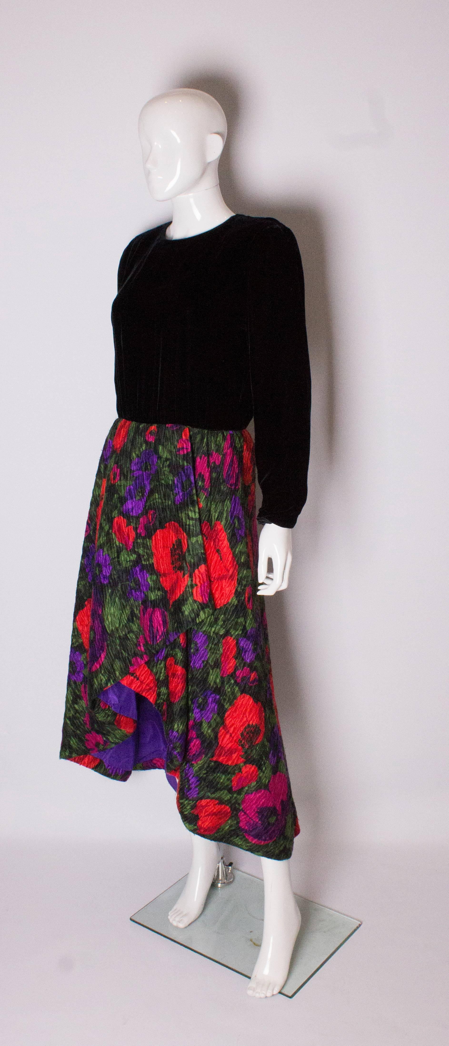 A chic evening dress by Akris. The dress has a black velvet body with a 5 button opening at the back. The the skirt is in a floral textured fabric , with purple lining, foldover at the front and zip opening at the rear.