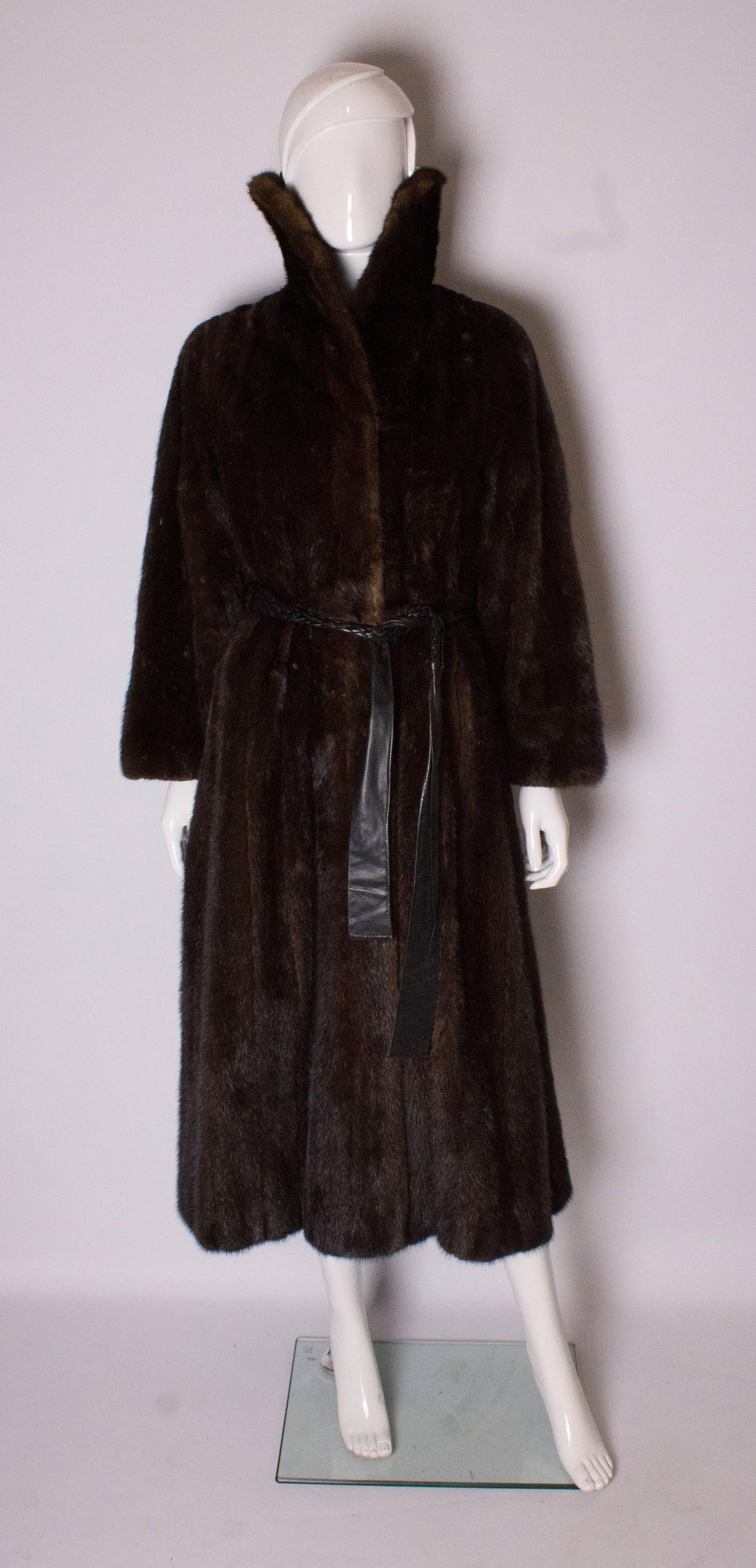 A glamorous mink coat with shawl collar and wrap over front. The coat has wide sleeves and a brown plaited leather belt ( coat has belt holes) that gives it definition.