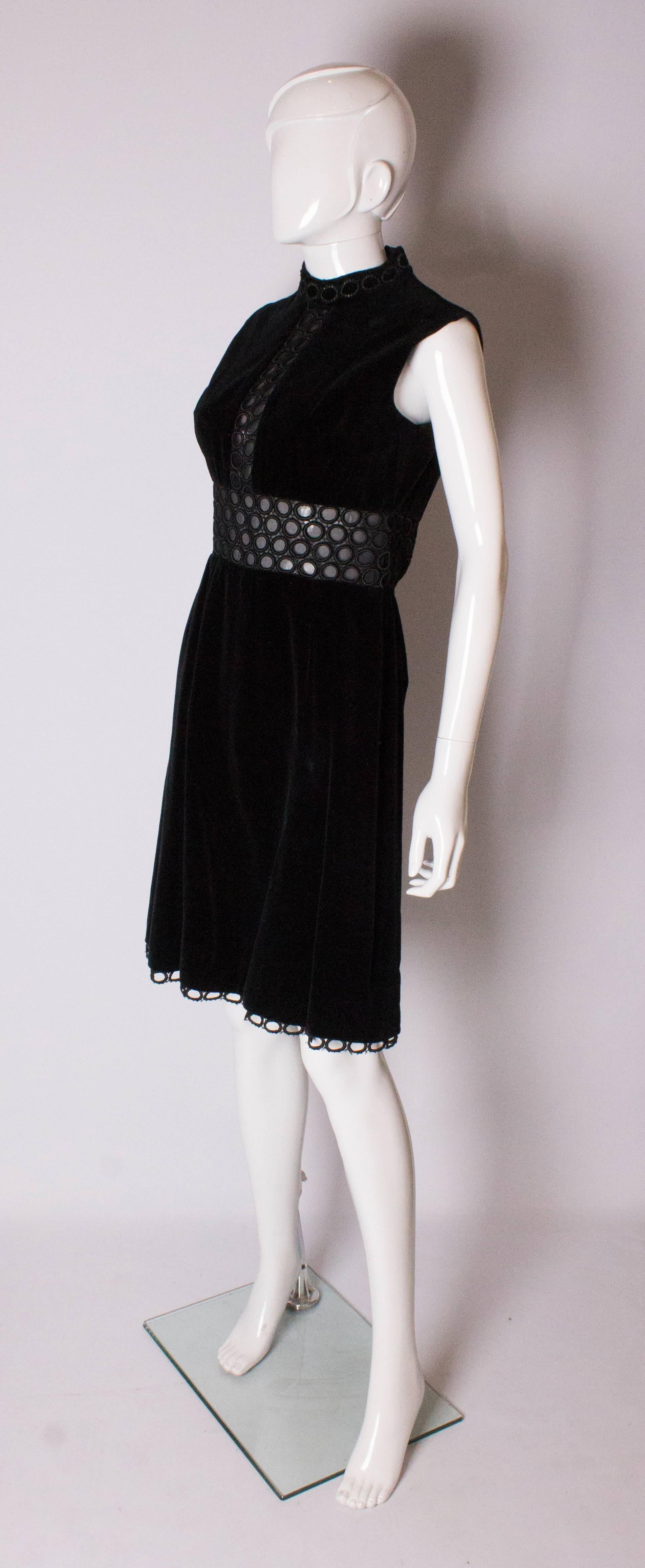 A chic cocktail dress by British designer Susan Small. The dress has a cut out mid panel and braiding around the neck and hem, with a central back zip.