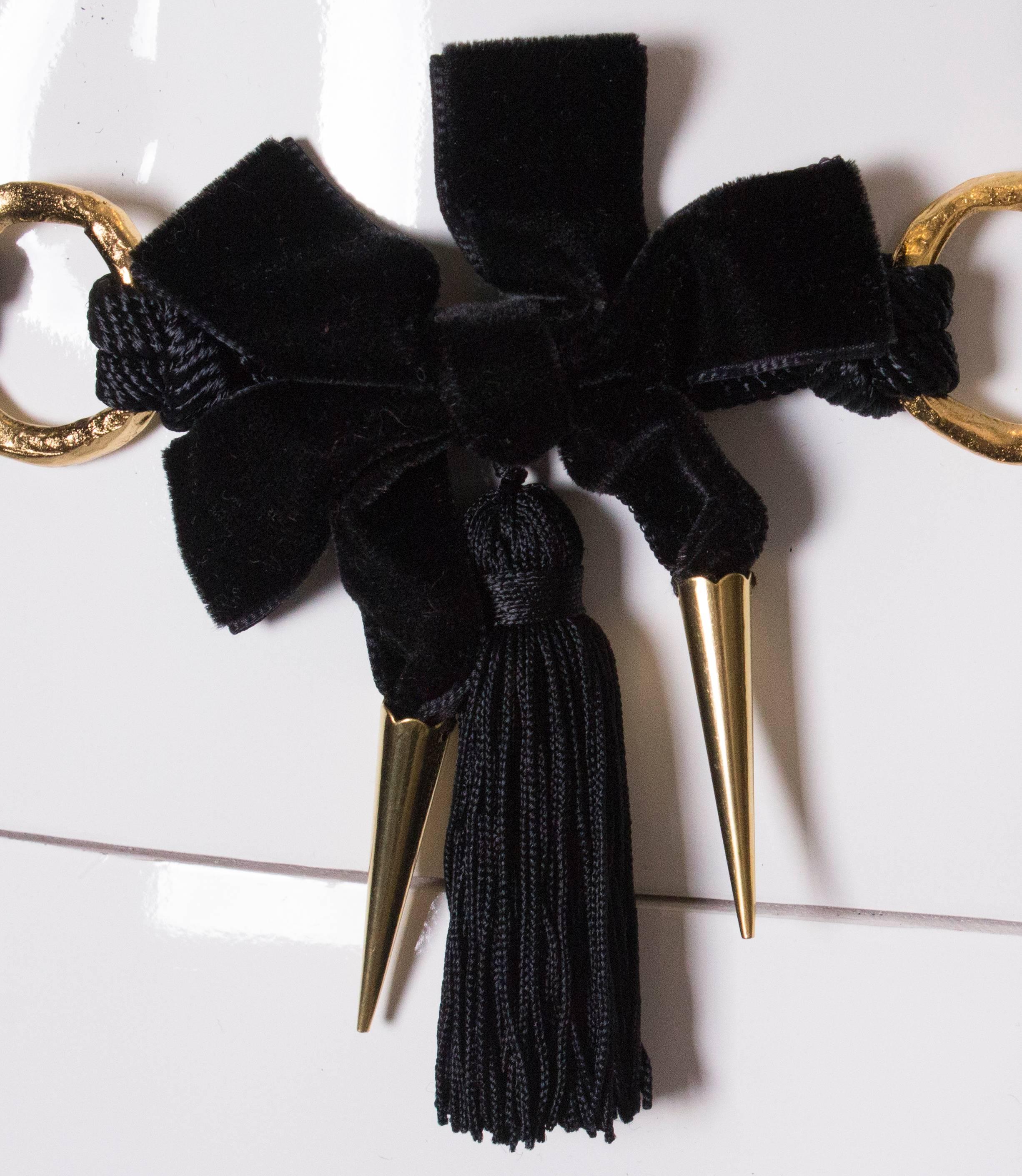 A great belt by Yves Saint Laurent. The belt is made of gold chain links with black velvet bows between each link. The bow have a tassle and two pointers below each bow. At the end of the body of the belt is a double cord 20'' in length. The total