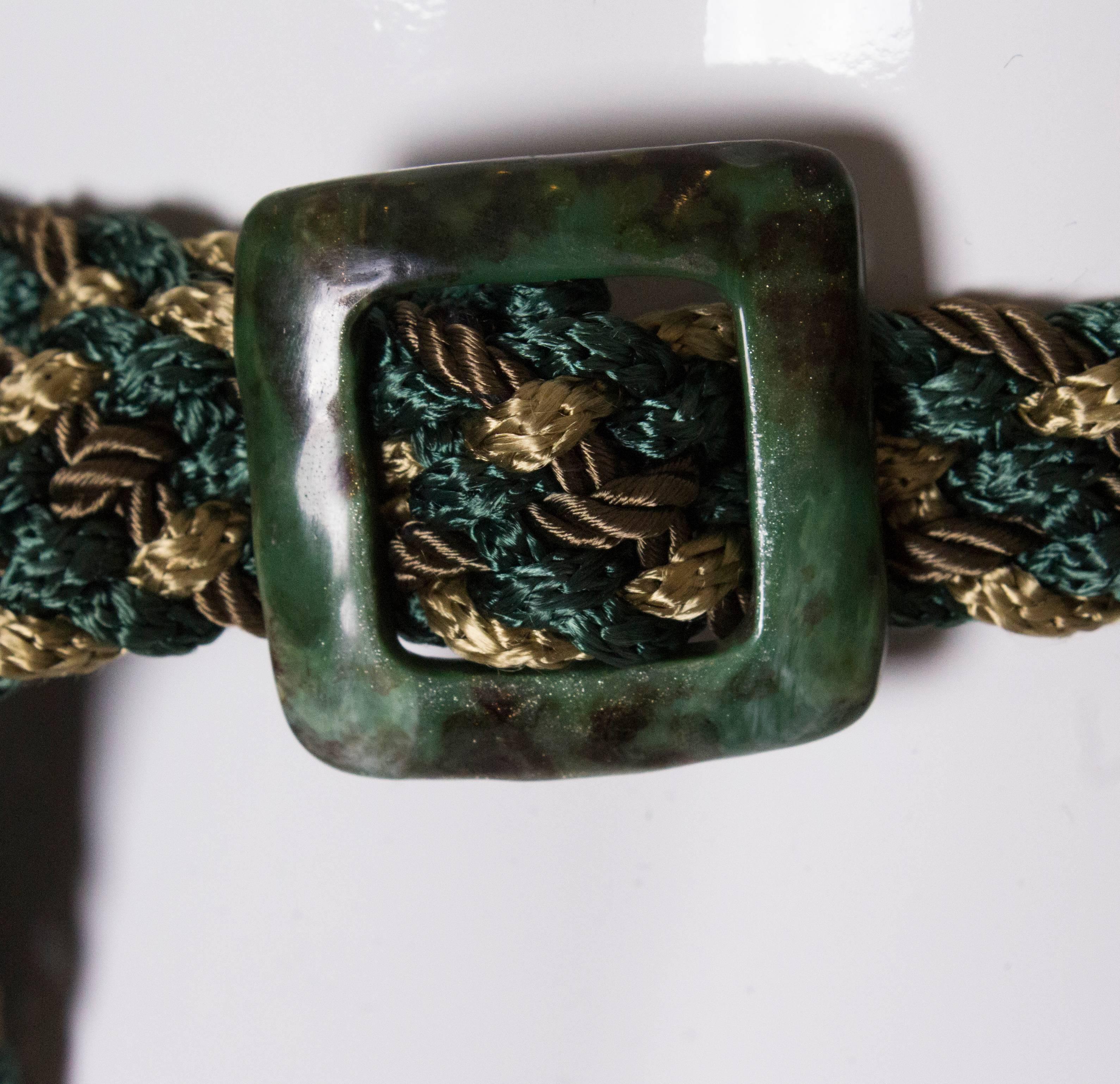 A great belt by Yves Saint Laurent. The belt is made of silk cord in green, gold and bronze with a green marble like buckle. The belt has no holes , so can work around you. It has a YSL gold tag.