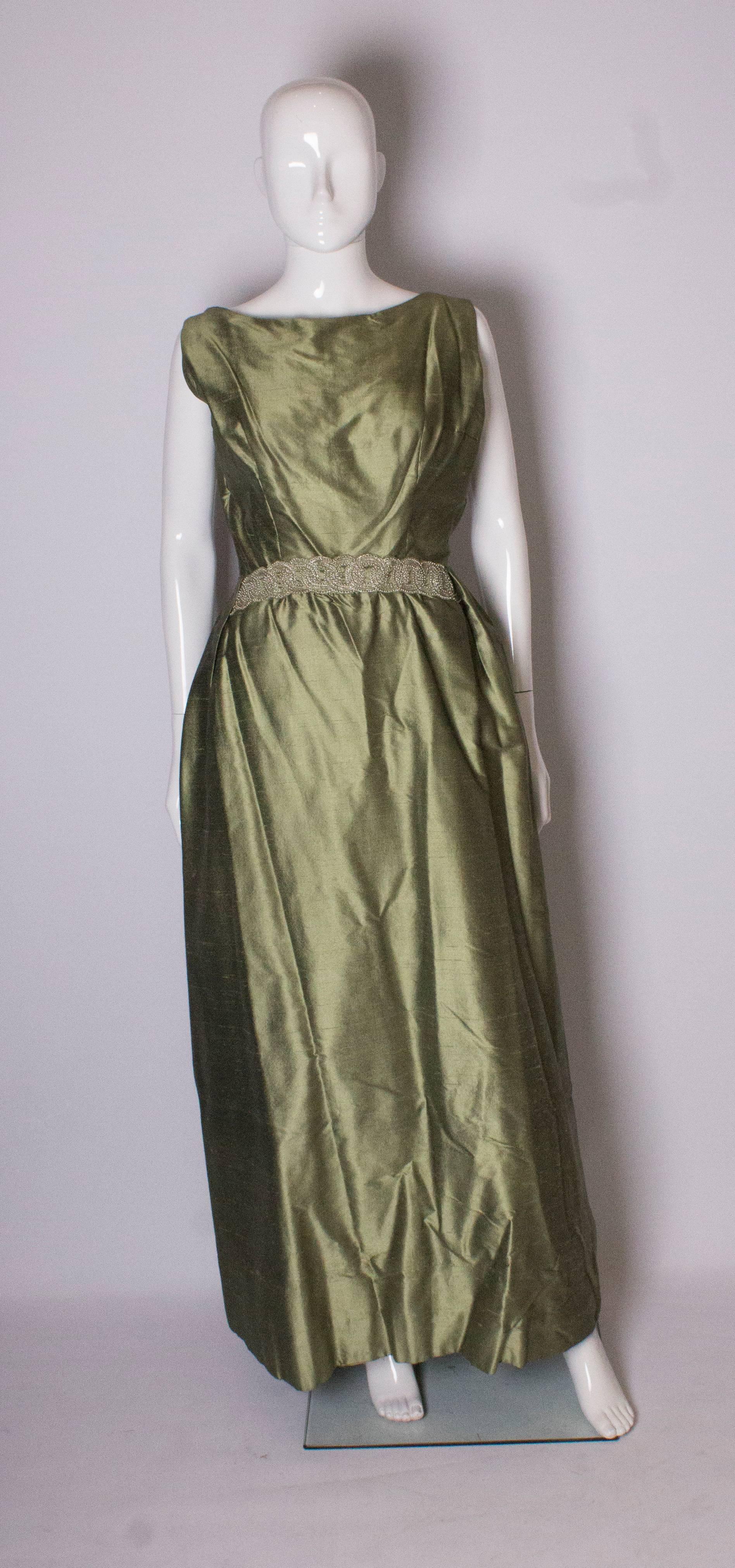 A pretty sage green silk ball gown /evening gown by Muriel Martin. The gown has a boat neckline at the front, and a square backneckline. There is a pretty beaded band that goes in and out at waist leval. It is fully lined with burgundy net and sage