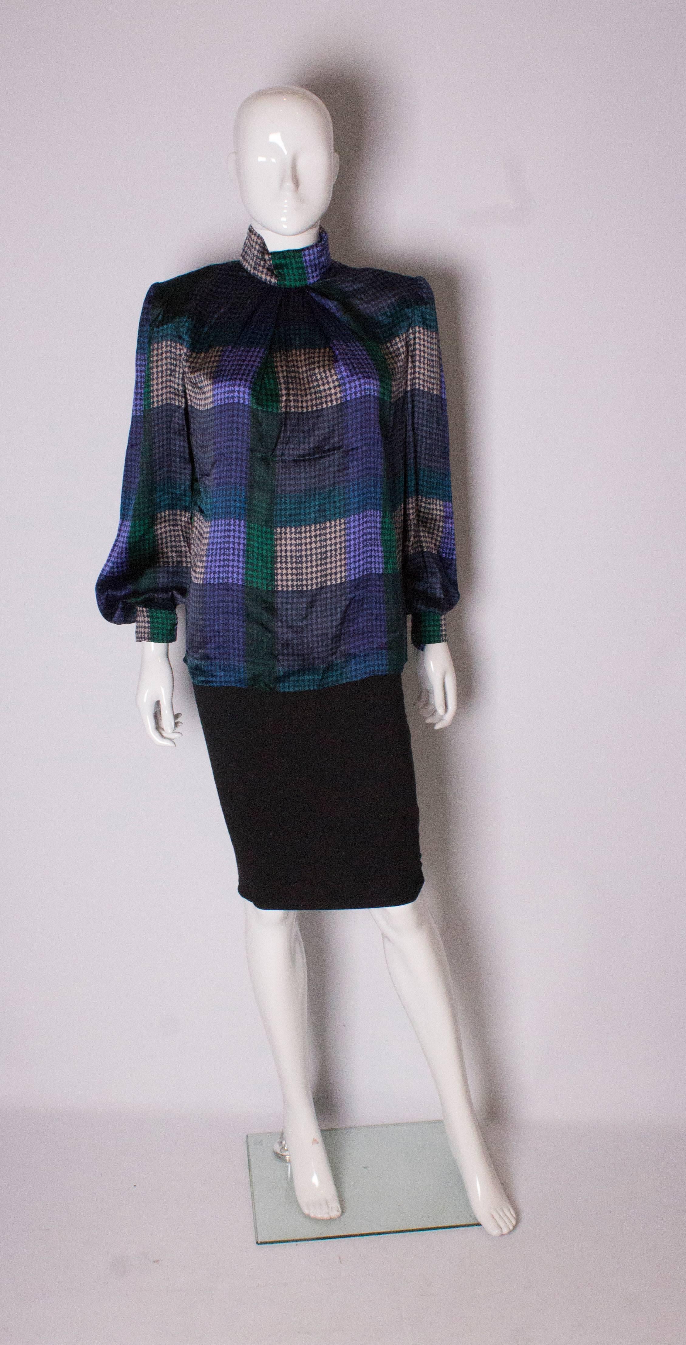 A chic silk blouse by Donald Campbell. In a hounds tooth print, in grey, green , purple and black. The blouse has a stand up collar, zip back and popper cuffs. 