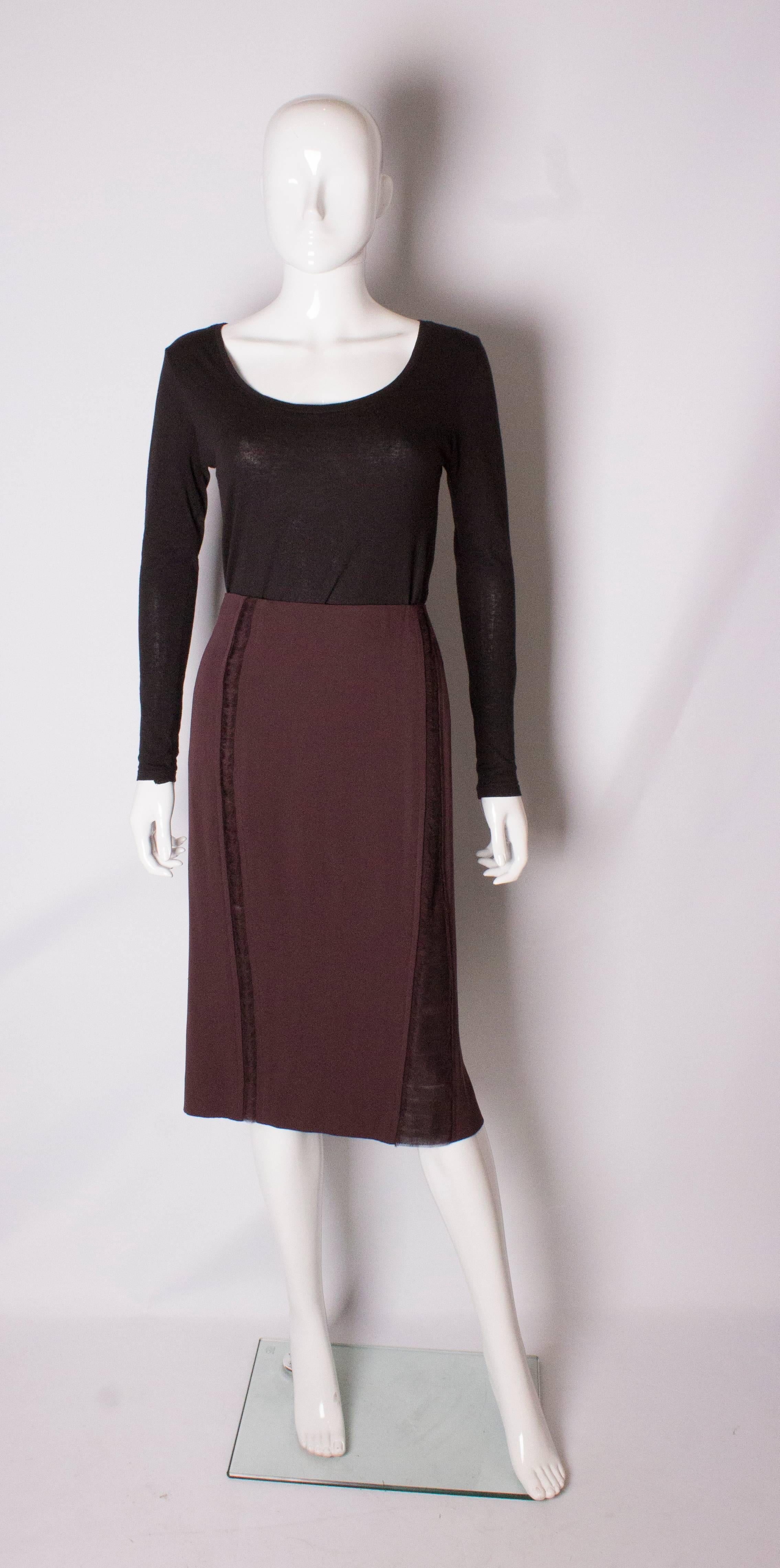 A chic skirt by Yves Saint Laurent , Rive Gauche line.  In a plum coloured silk, the skirt has a net panel down the centre front, and a net panel and frill on either side . It has a central back zip, with a 7'' slit at the back.