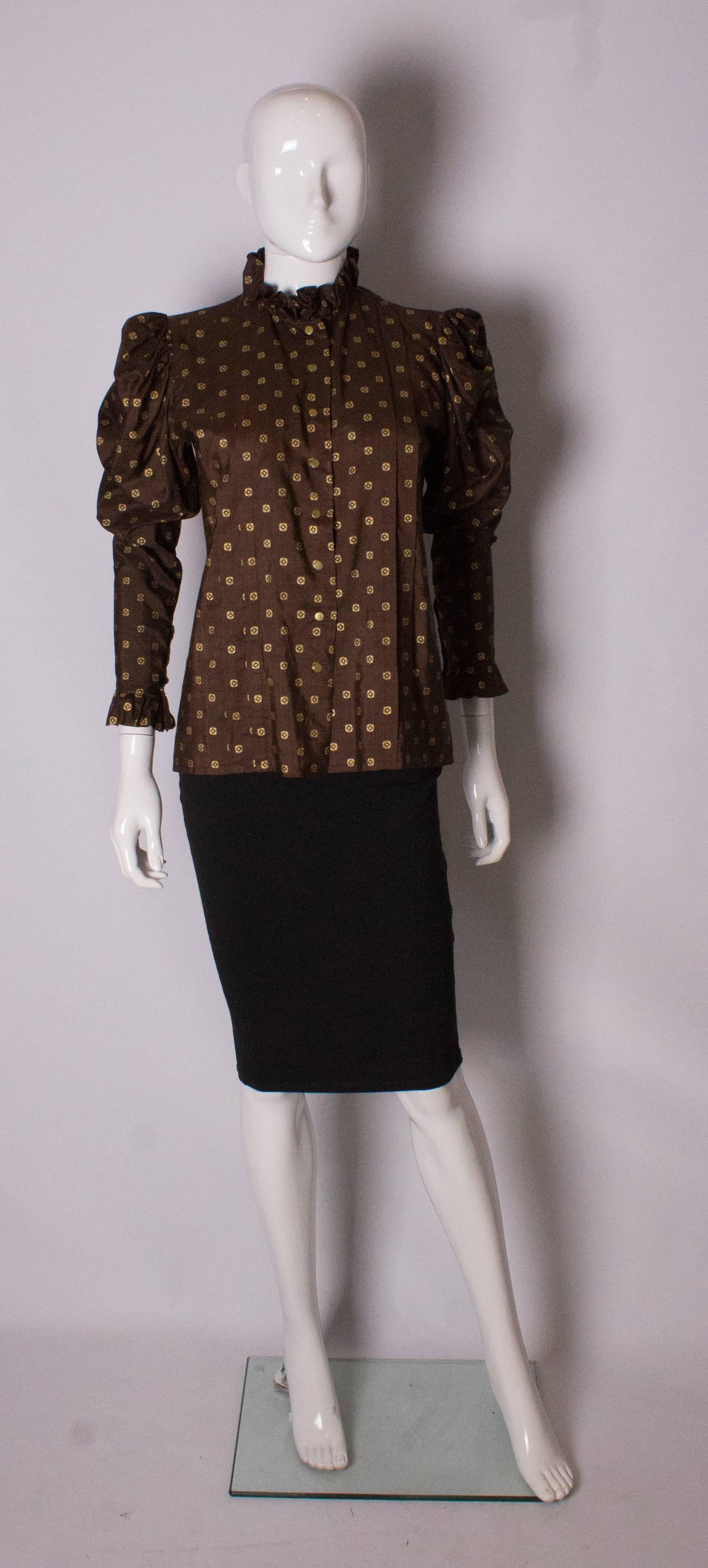 A stunning blouse, by Yves Saint Laurent Rive Gauche. The blouse is in brown silk with gold floral detail. It opens with gold poppers at the front and vertical pleats to either side.There is a frill at the neck and the cuffs, and gathering on the