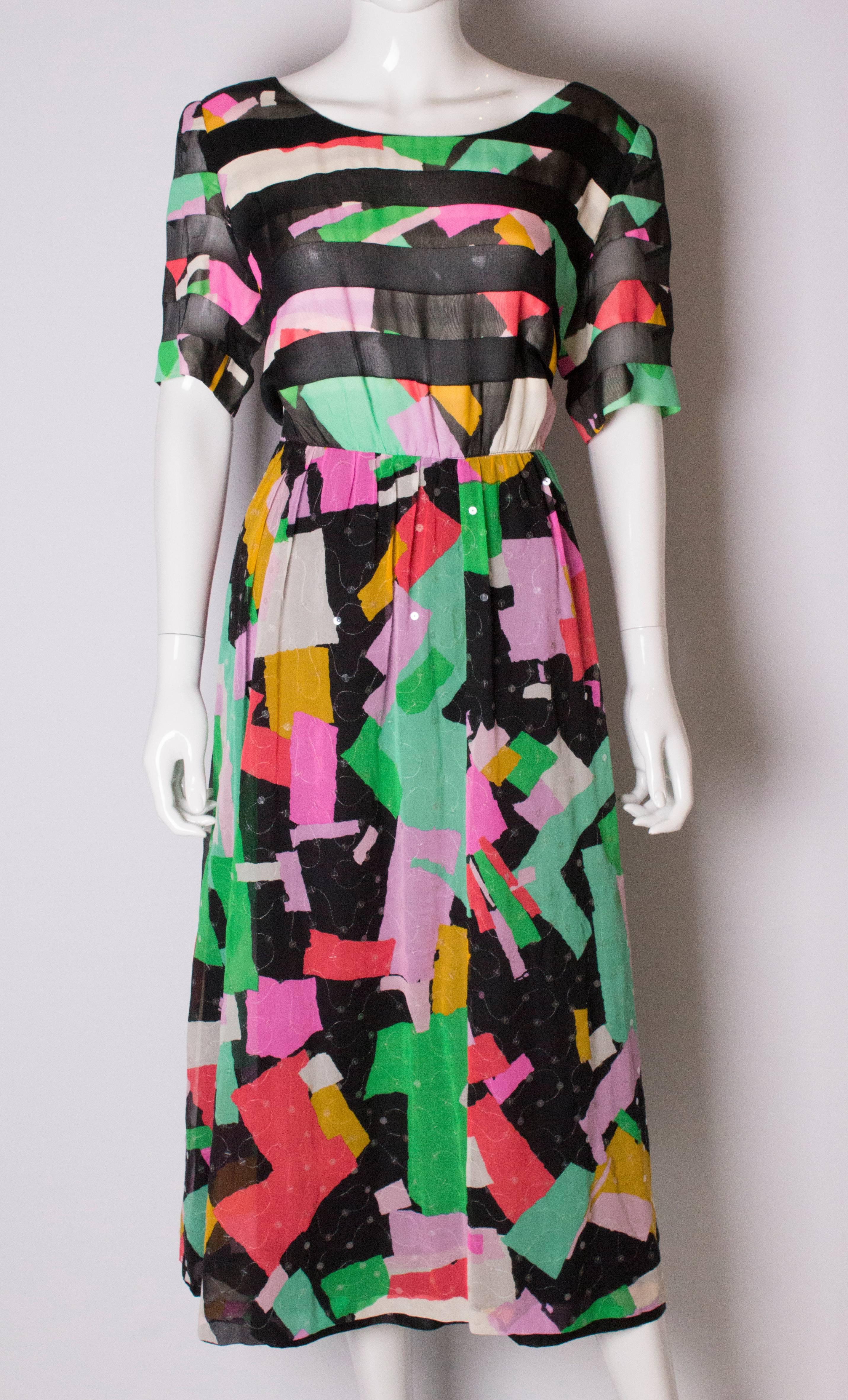 A pretty silk dress by Donald Campbell. The dress is multi coloured with clear sequins attached.  It has a round neck with sheer panels in the bodice and short sleeves. It is gathered at the waist and fully lined.