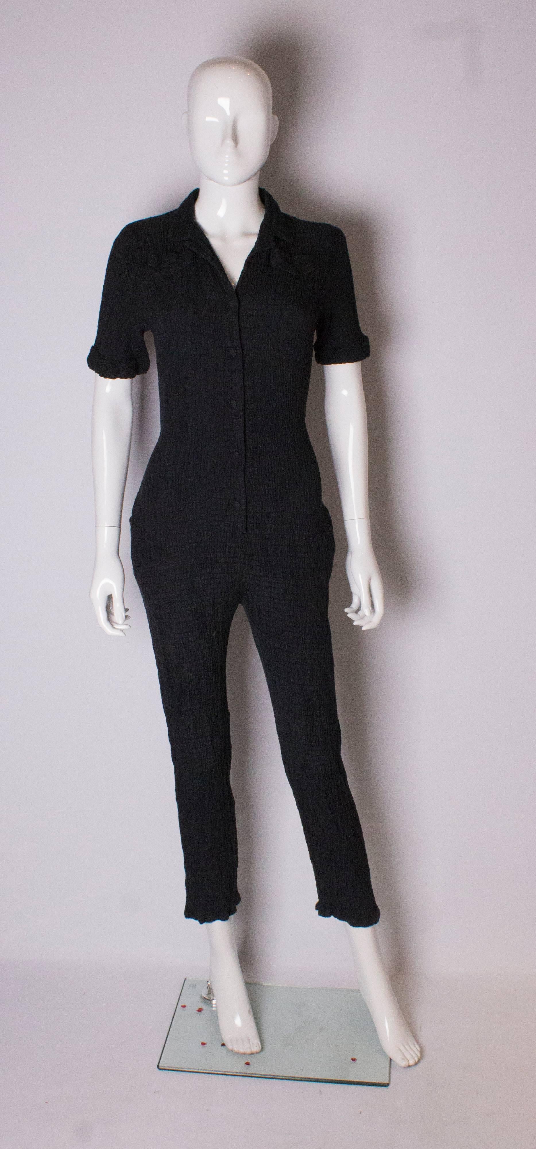 A chic black jumpsuit from Gail Hoppen. In a textured fabric the jumpsuit has a 5 button front opening, with a small breast pocket on either side. It has an elasticated waist and pockets at either side  at hip leval.  Measurements: bust 34'', length