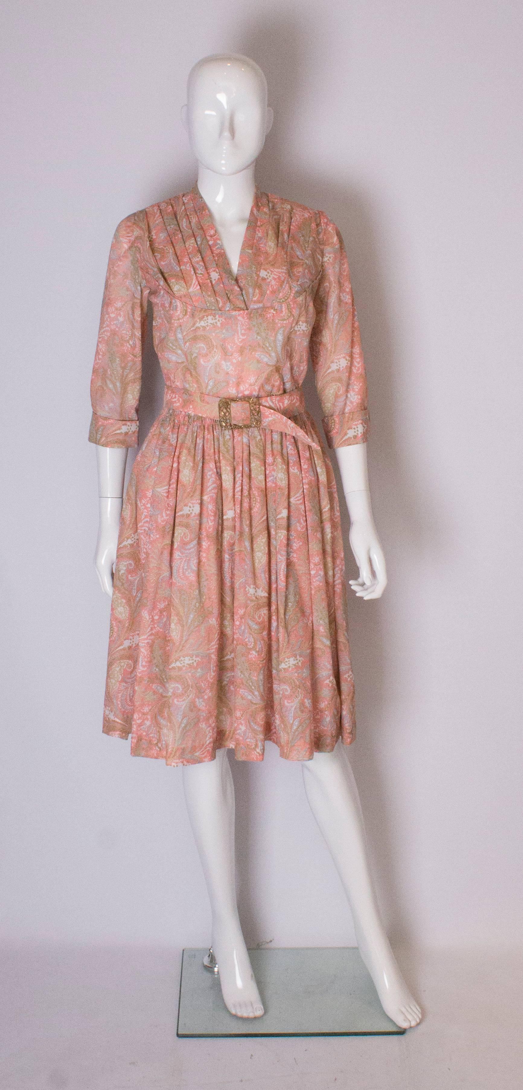 A pretty floral day dress with a v neckline with folds detail, and elbow length sleeves with cuffs . It has an elasticated waist  for easy wearing, and the dress has a self fabric belt with decorative buckle.