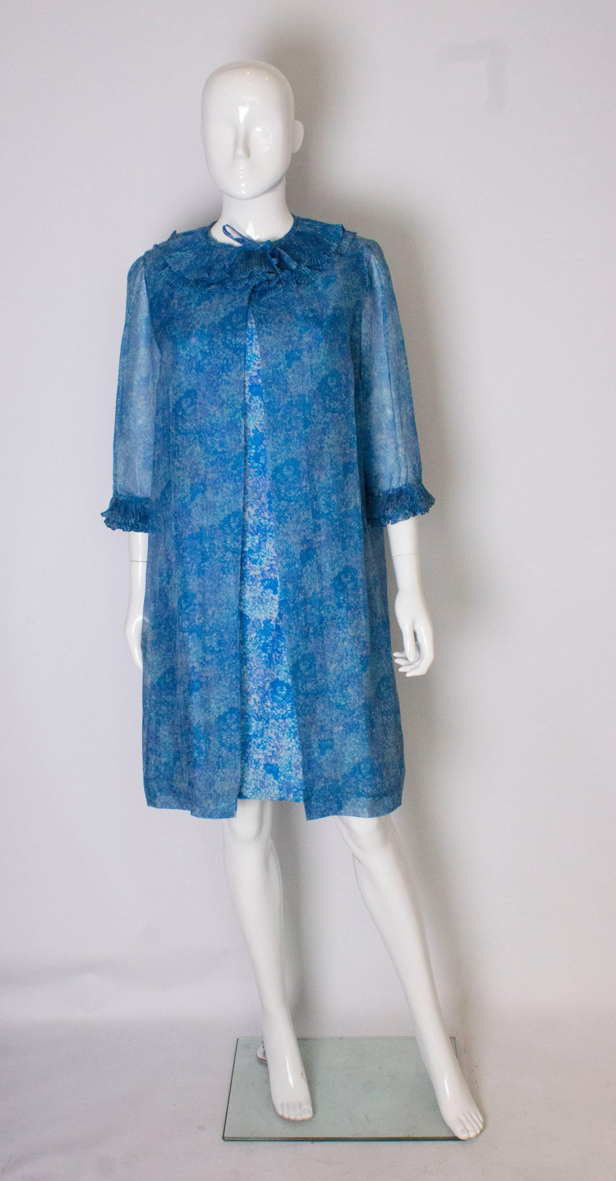 A pretty cocktail dress with matching long jacket. The dress has an ivory background with a blue floral print. It has a deep v back line with fabric covered buttons and is fully lined. The coat is loose fitting and light , and has two rows of