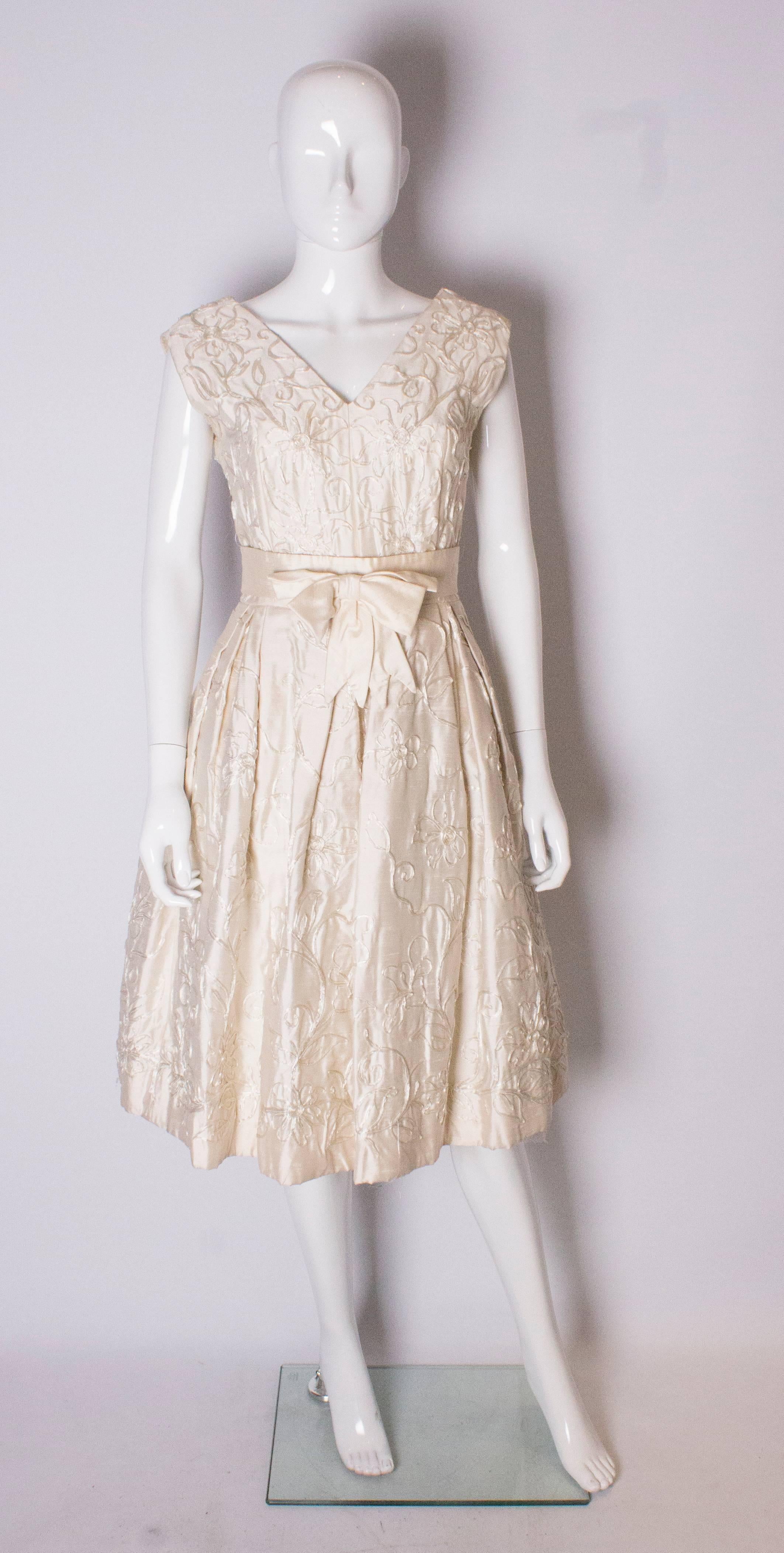 A wonderful 1950s cocktail dress or possible wedding dress. The dress is in an ivory silk mix fabric, with ribbon detail. The dress has a v neckline front and back, with a central back zip and two layers of lining underneath to create a great skirt.
