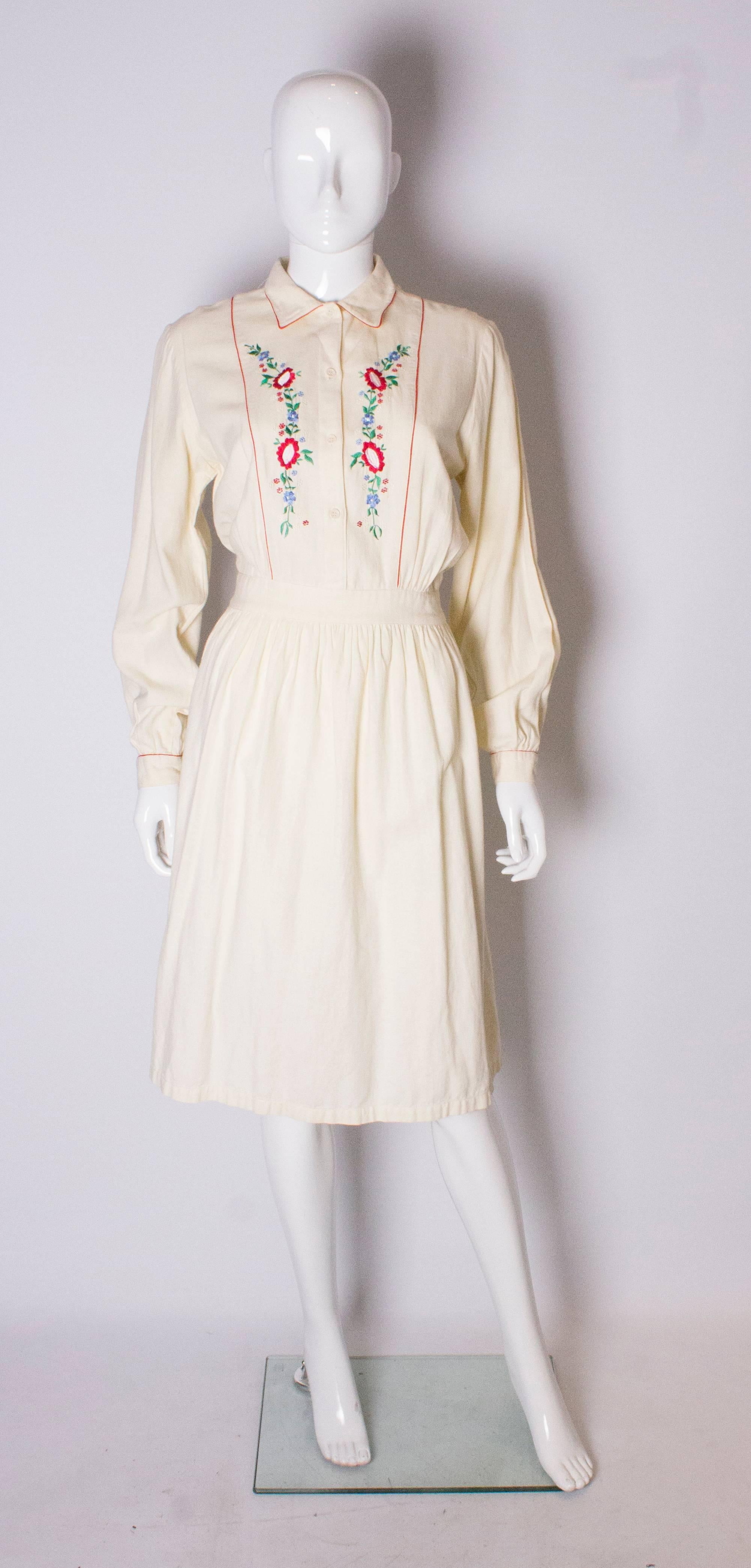 A pretty vintage day dress by Miss Selfridge. The dress is in an ivory brushed cotton with embroidery on the front , and red piping on the collar and cuffs.The dress has a 4  button opening at the front and self fabric tie backs, so can be adjusted