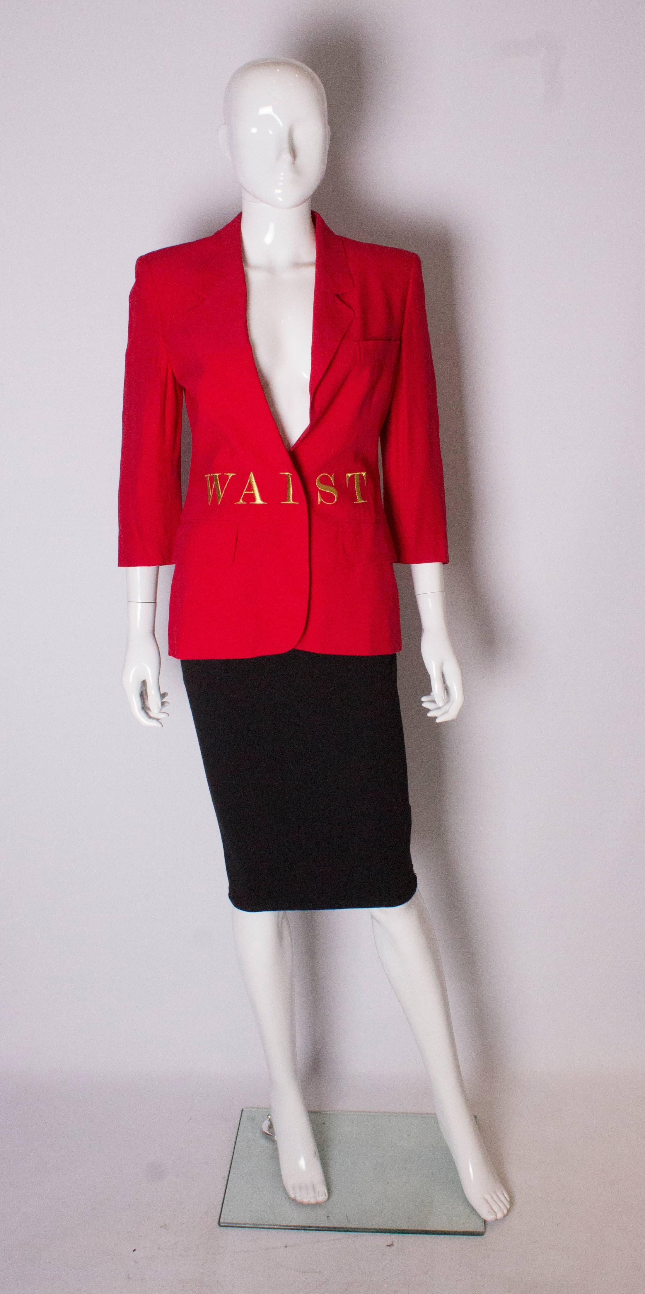 A chic vintage couture jacket by Moschino. The jacket is in a red fabric and embroidered with 'waist of money'  in gold around the waist. The jacket fastens with two poppers, and has decorative buttons on each cuff.