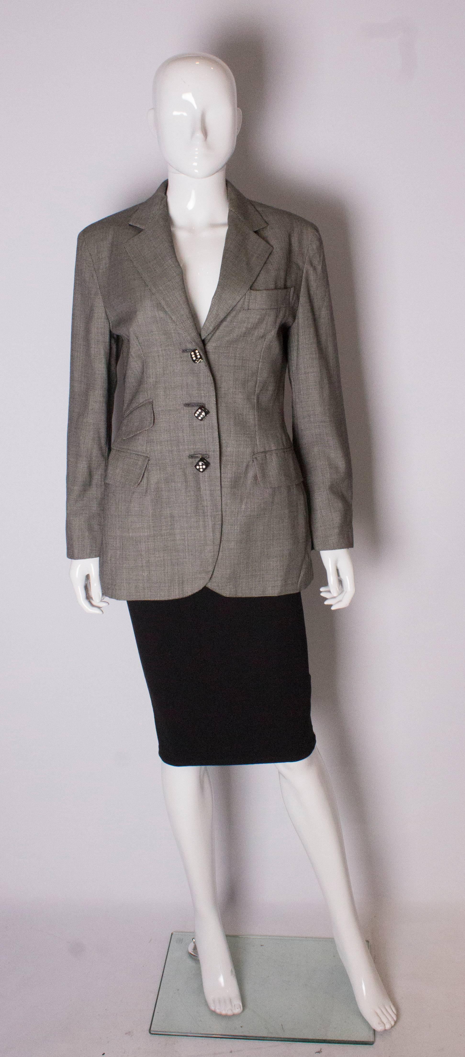 A chic jacket by Moschino Couture. The jacket is in a black and white wool fabric with a red lining. The jacket  has a pocket at breast leval on the left hand side, and two pockets on the right hand side. The jacket has three decorative dice like