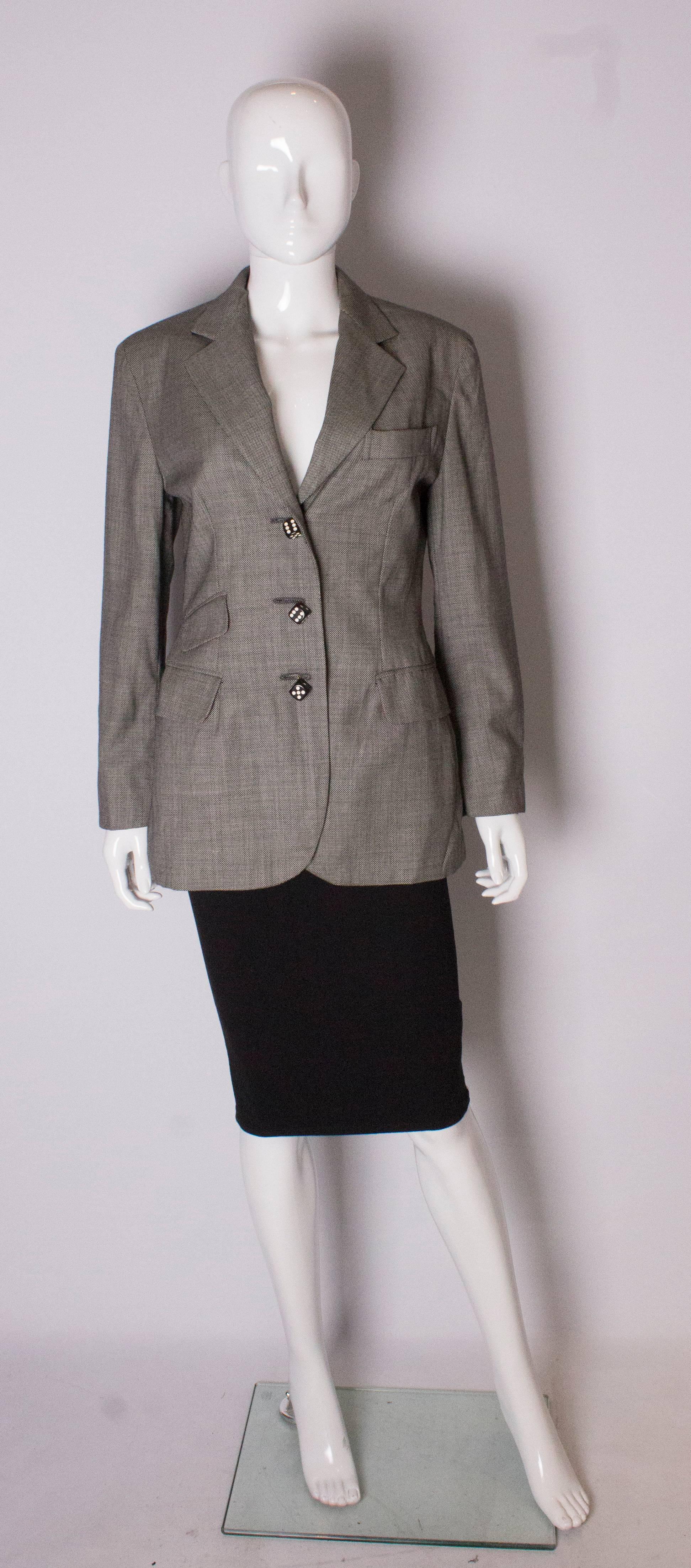 Una chaqueta chic de Moschino Couture. La chaqueta es de un tejido de lana blanco y negro con forro rojo. La chaqueta  Tiene un bolsillo en el pecho en el lado izquierdo y dos bolsillos en el lado derecho. La chaqueta tiene tres botones decorativos