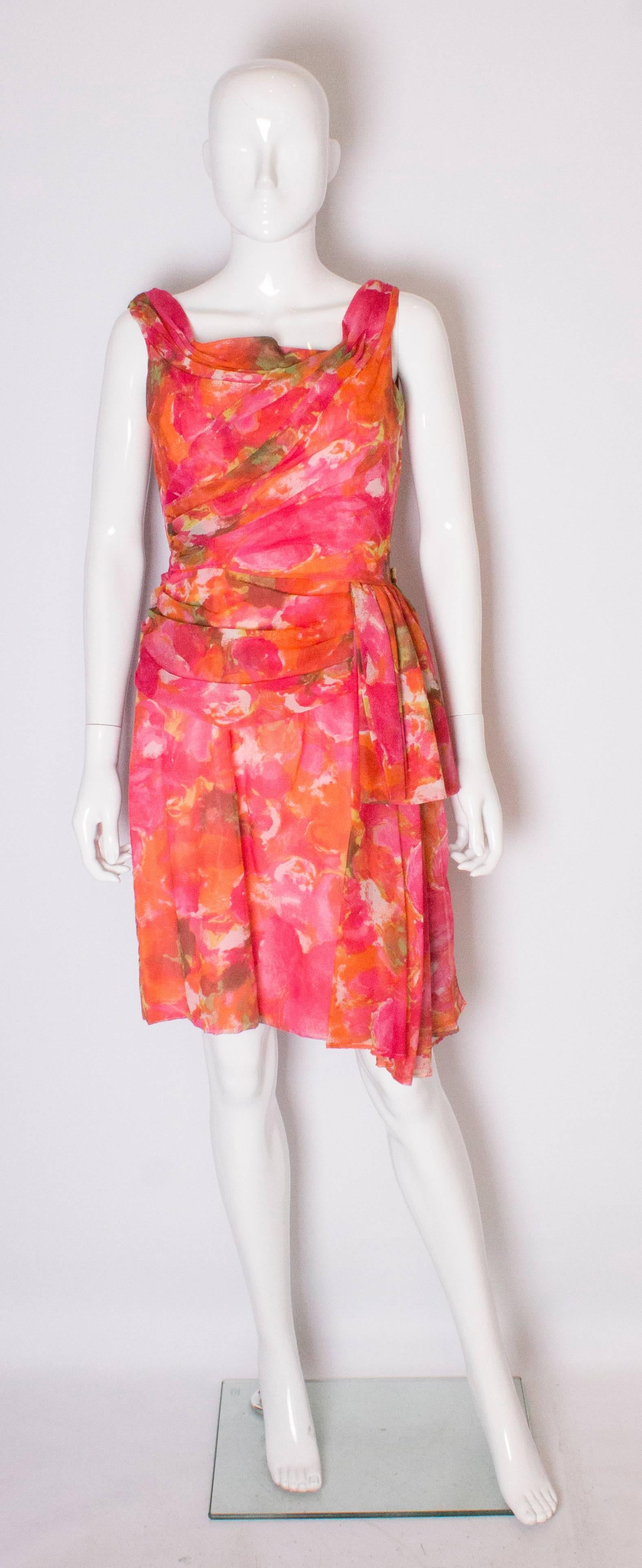 A pretty cocktail dress by London Town , Mayfair.  The dress is a colourful mix of pinks ,orange and red. It has drapes at the front and back and ties at the waist. It has a central back zip, and 3''hem.

