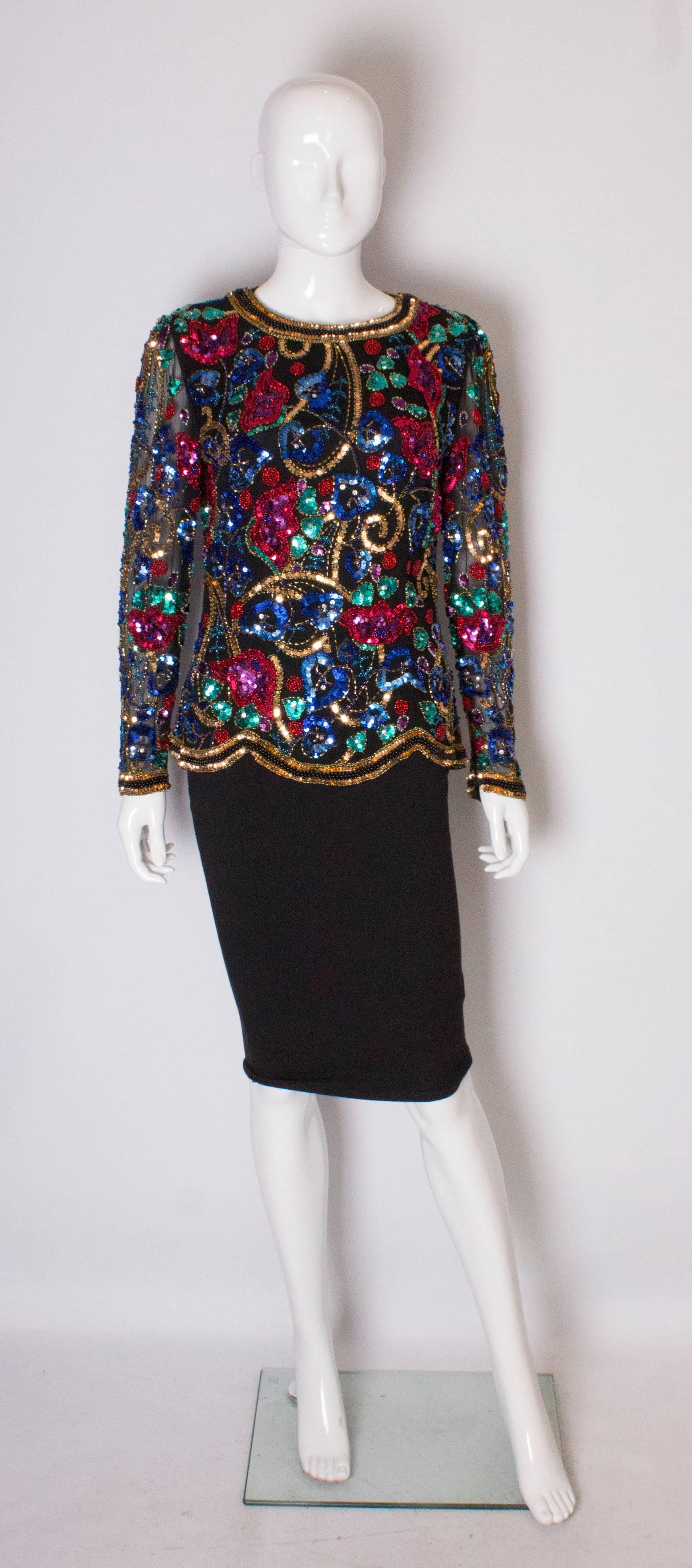 A pretty beaded evening top by Oleg Cassini Black Tie Line. The top has a black background with gold sequins areound the neck, hem and cuffs.The top  has a round neckline, central back zip, fully lined body and sheer sleeves. It is wonderfuly