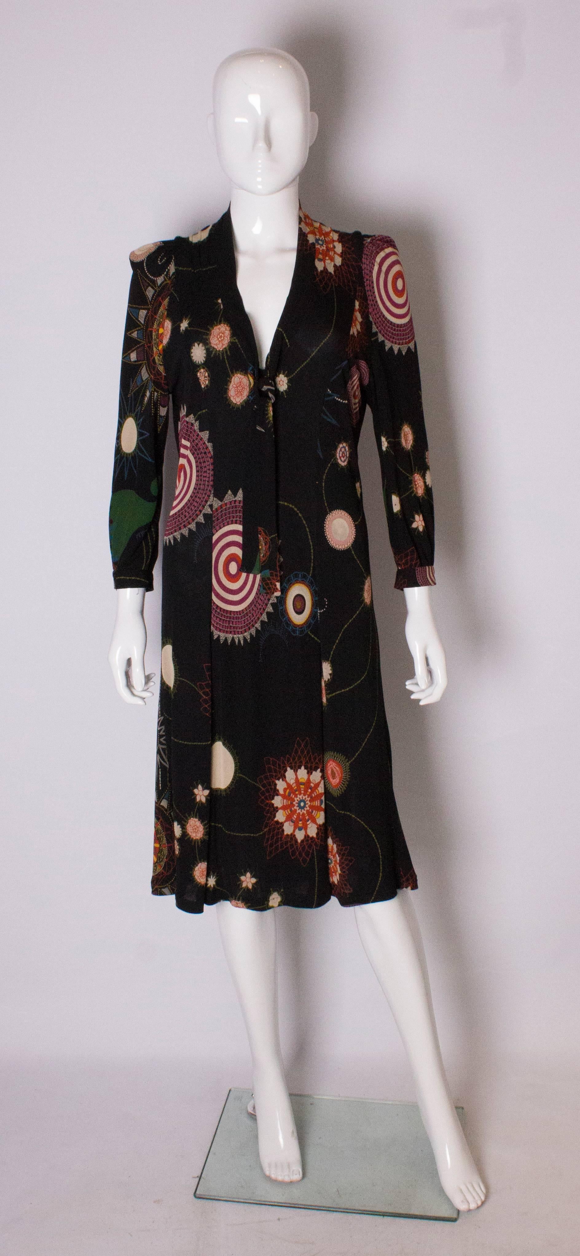 A chic and easy to wear   dress by Christian Lacroix, Bazaar line. The dress has a  black background with  a mulit coloured print. It has pleats on the shoulder and v neck with a tie neck that can be worn tied or loose. The dress has a side zip