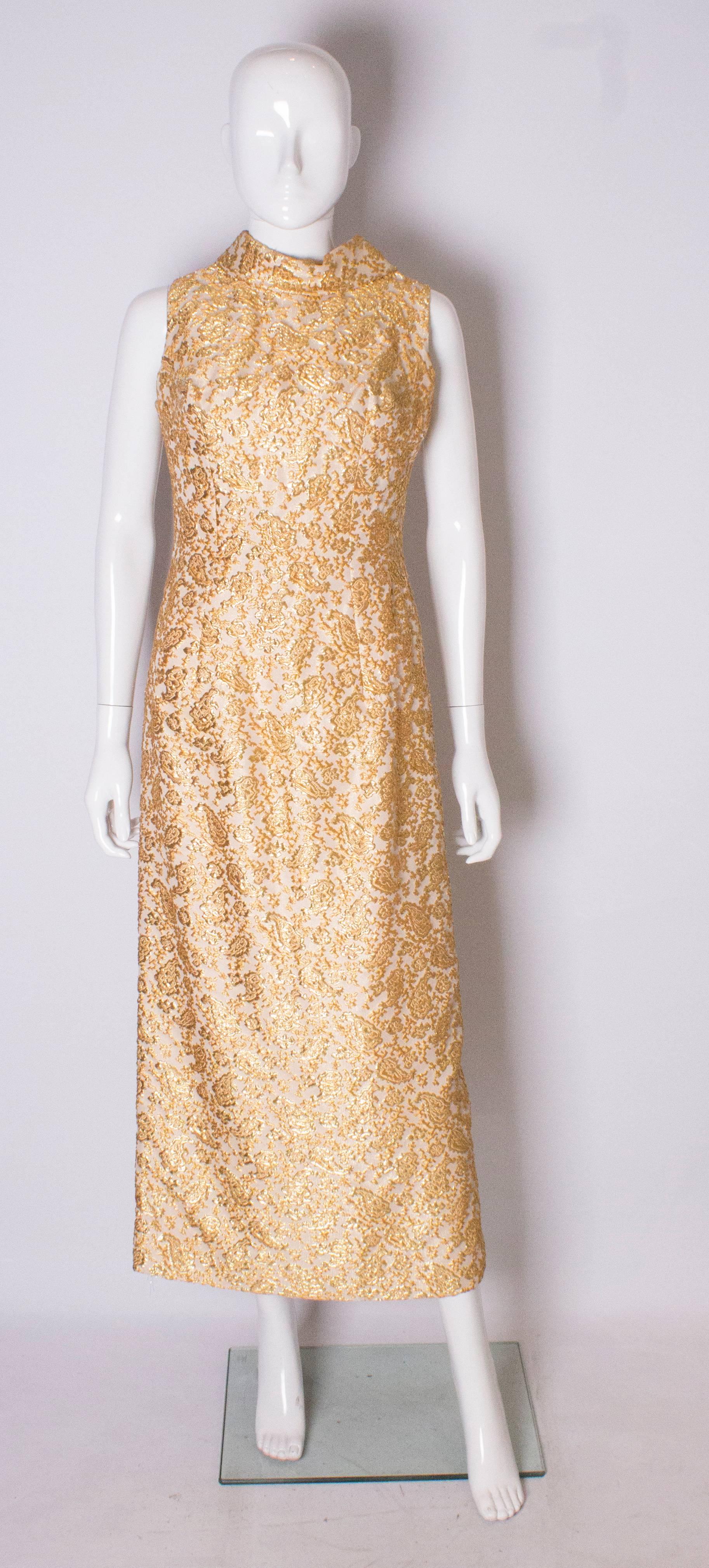 A chic full length sleaveless evening gown, in  a gold brocade like fabric. The dress is fully lined with a central back zip , and has a  fold over collar.