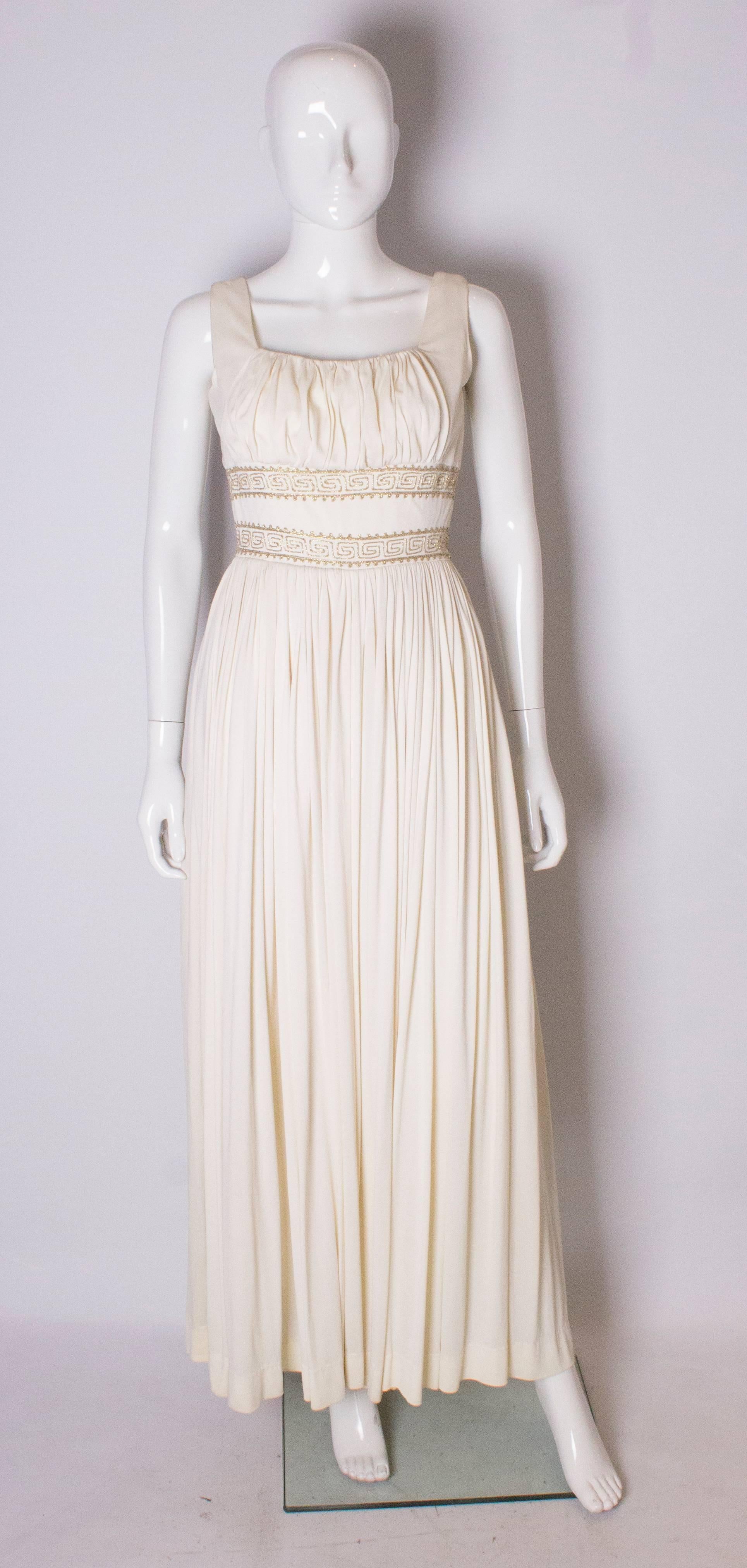 A chic white Grecian style evening gown. The dress has a scoop neckline with gathering over the bust with two rows of gold braiding under the bust,and a full skirt. The dress has a central back zip, and is fuly lined.