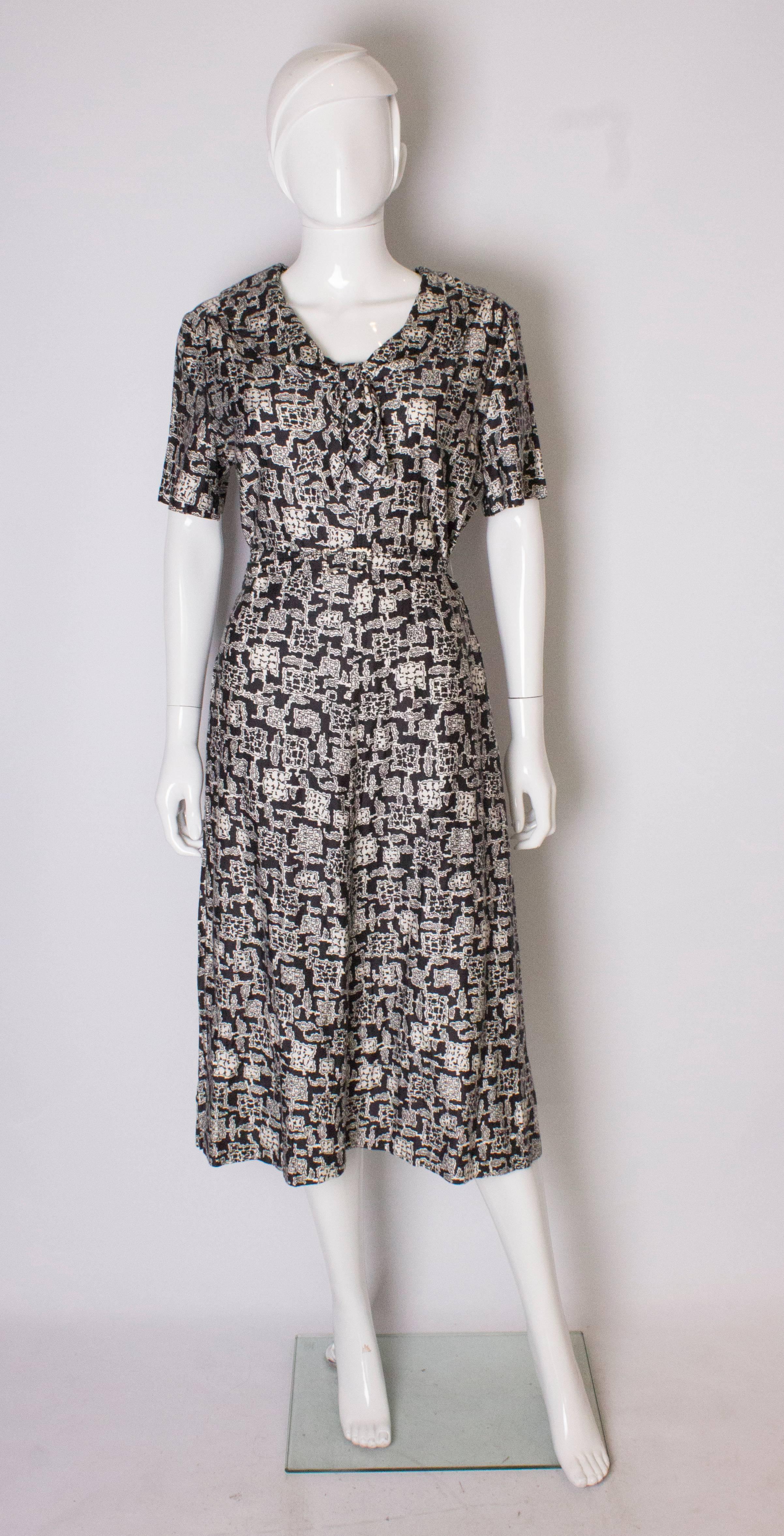 A stylish black and white printed vintage day dress by Horrockses .The dress has a v neckline with bow detail,  a self fabric belt at the waist, and central zip at the back. It is unlined. Bust up to 39'' ,length 47''