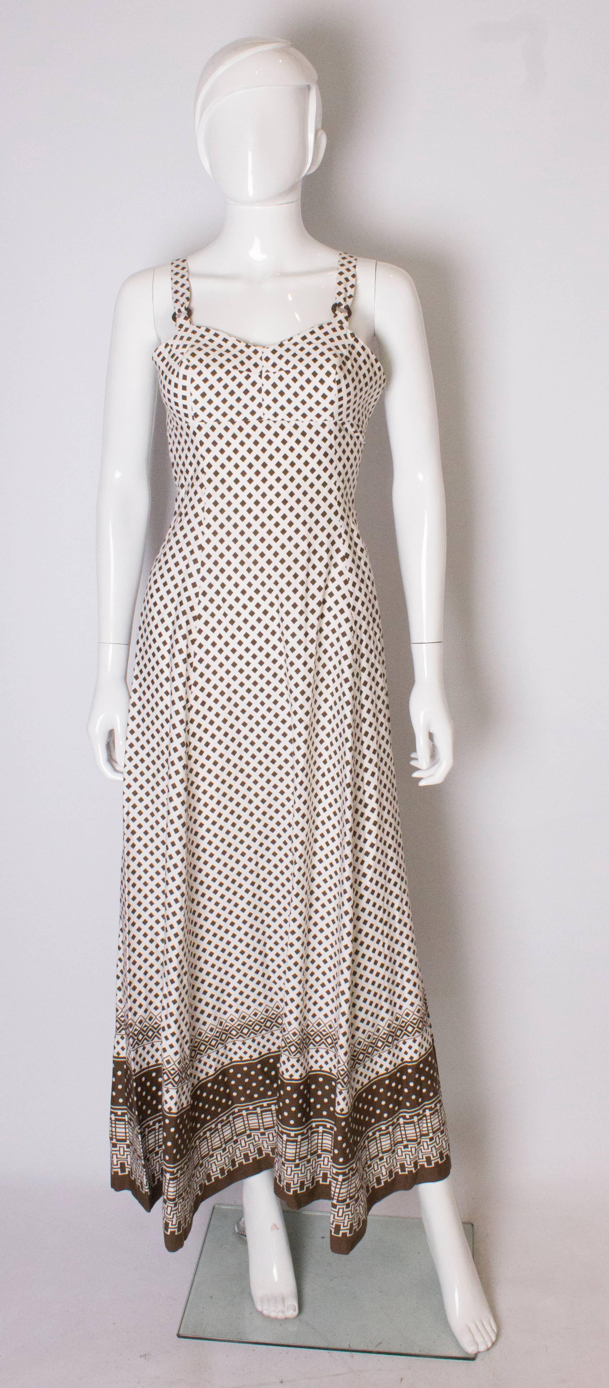 A chic gown for Summer by British firm, Horrockses. In a brown and white print, the dress has wide shoulder straps with decorative ring detail, and a decorative boarder at the hem. The dress has a side zip.