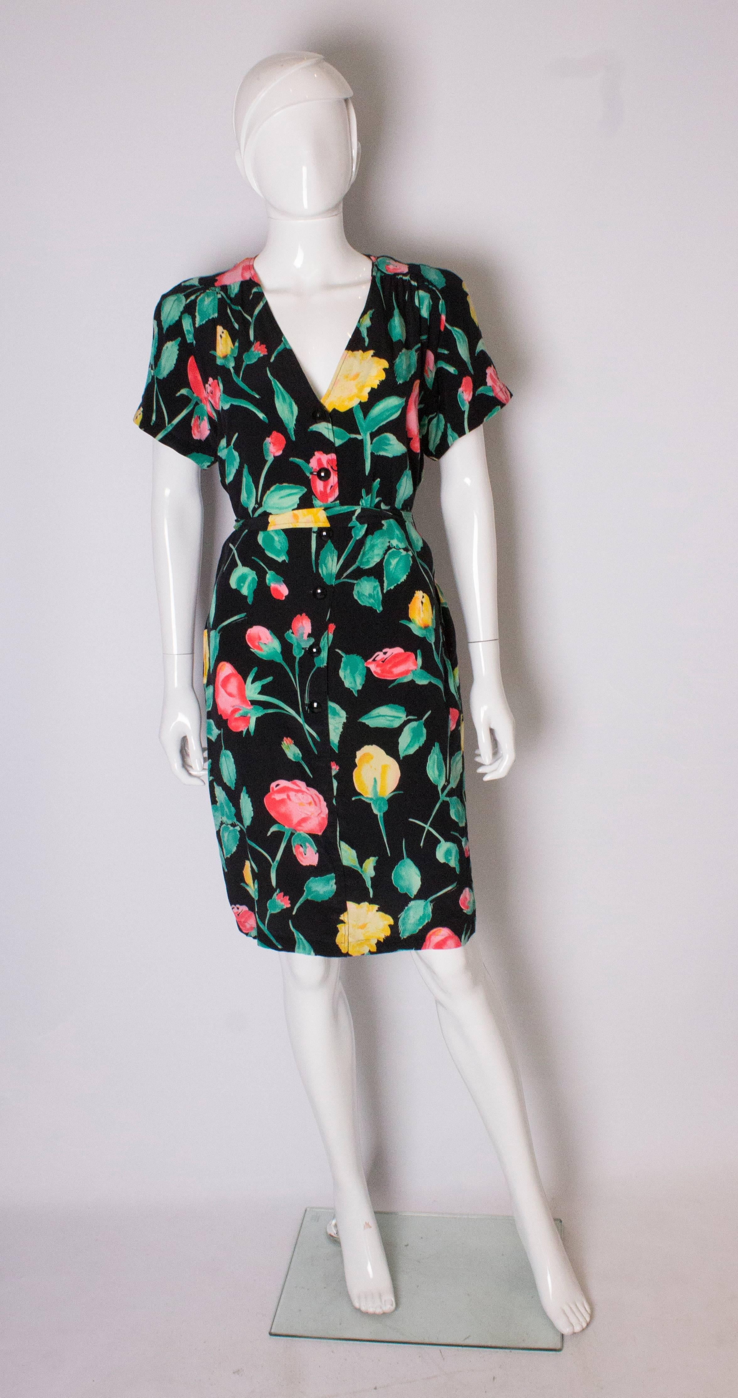 A chic silk  dress for Summer by Italian firm Ungaro. The dress is in silk,  and has a black background with a floral print in  yellow, green, red and pink. It has a v neckline, a self fabric belt , gathering at the shoulders and button through